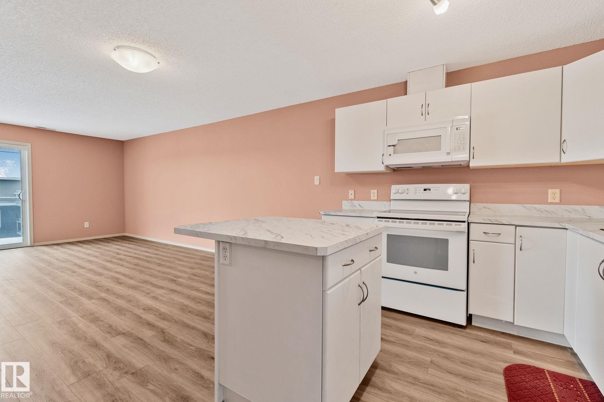 Kitchen featuring white appliances, light countertops, white cabinets, and a textured ceiling - 406 16035 132 Street Nw, Edmonton, AB - Indoor Photo Showing Kitchen
