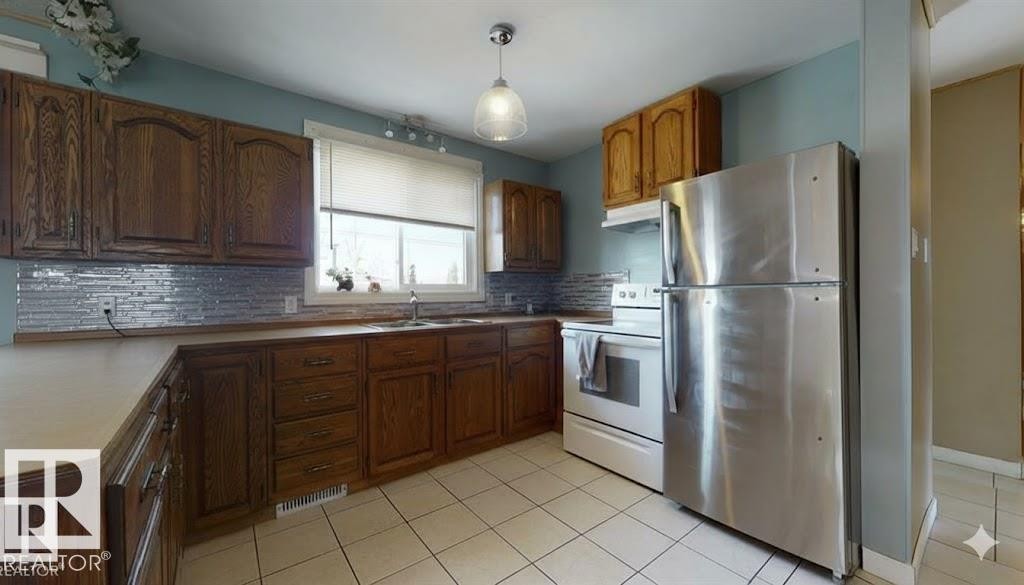 Kitchen featuring freestanding refrigerator, white electric range oven, light tile patterned flooring, light countertops, and wood finish cabinets - 4706 53 St, Leduc, AB - Indoor Photo Showing Kitchen With Double Sink