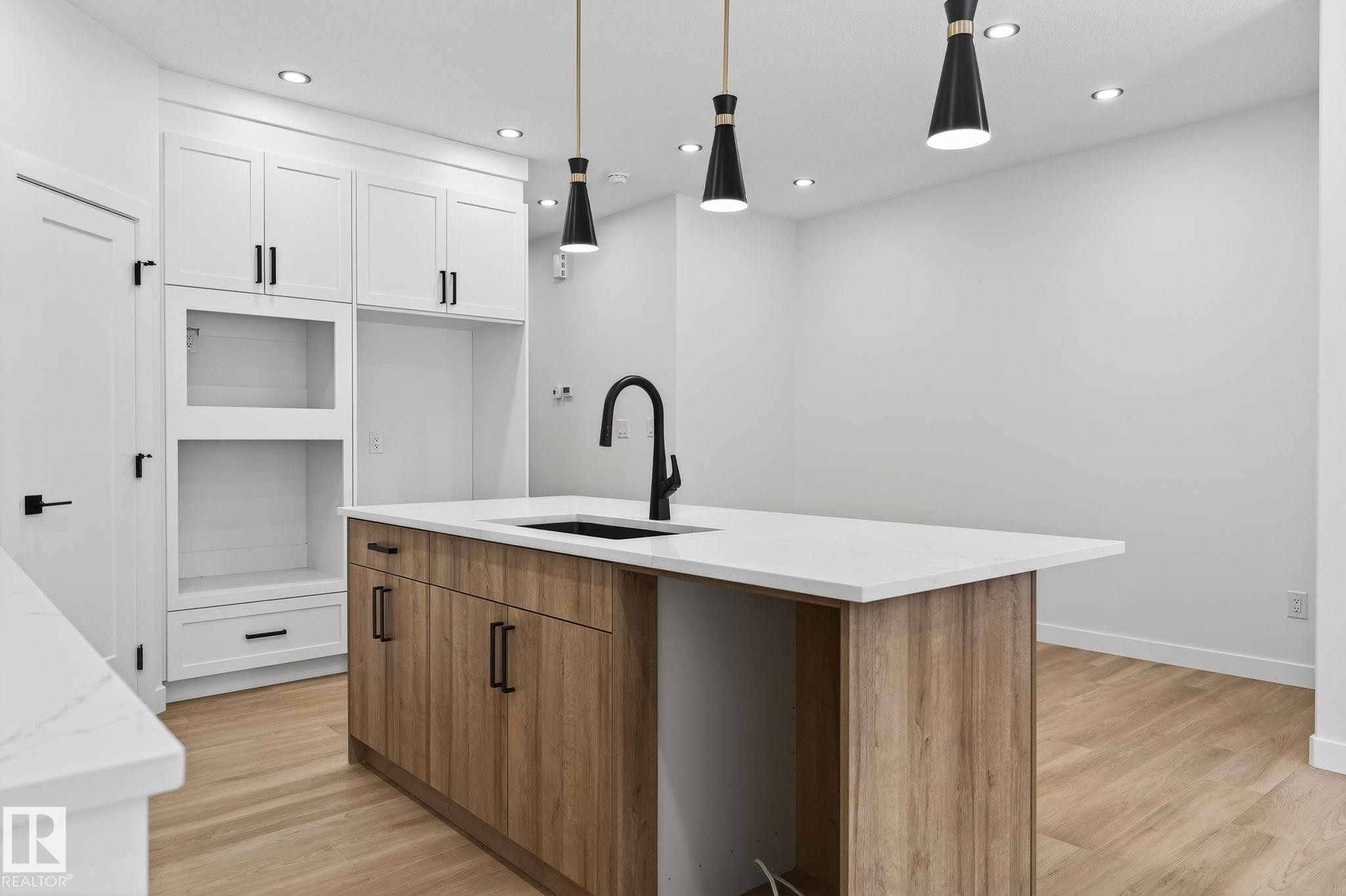 Two tone kitchen with two tone cabinetry, pendant lighting, light wood-style floors, a kitchen island with sink, and light stone counters - 3318 Chickadee Drive, Edmonton, AB - Indoor