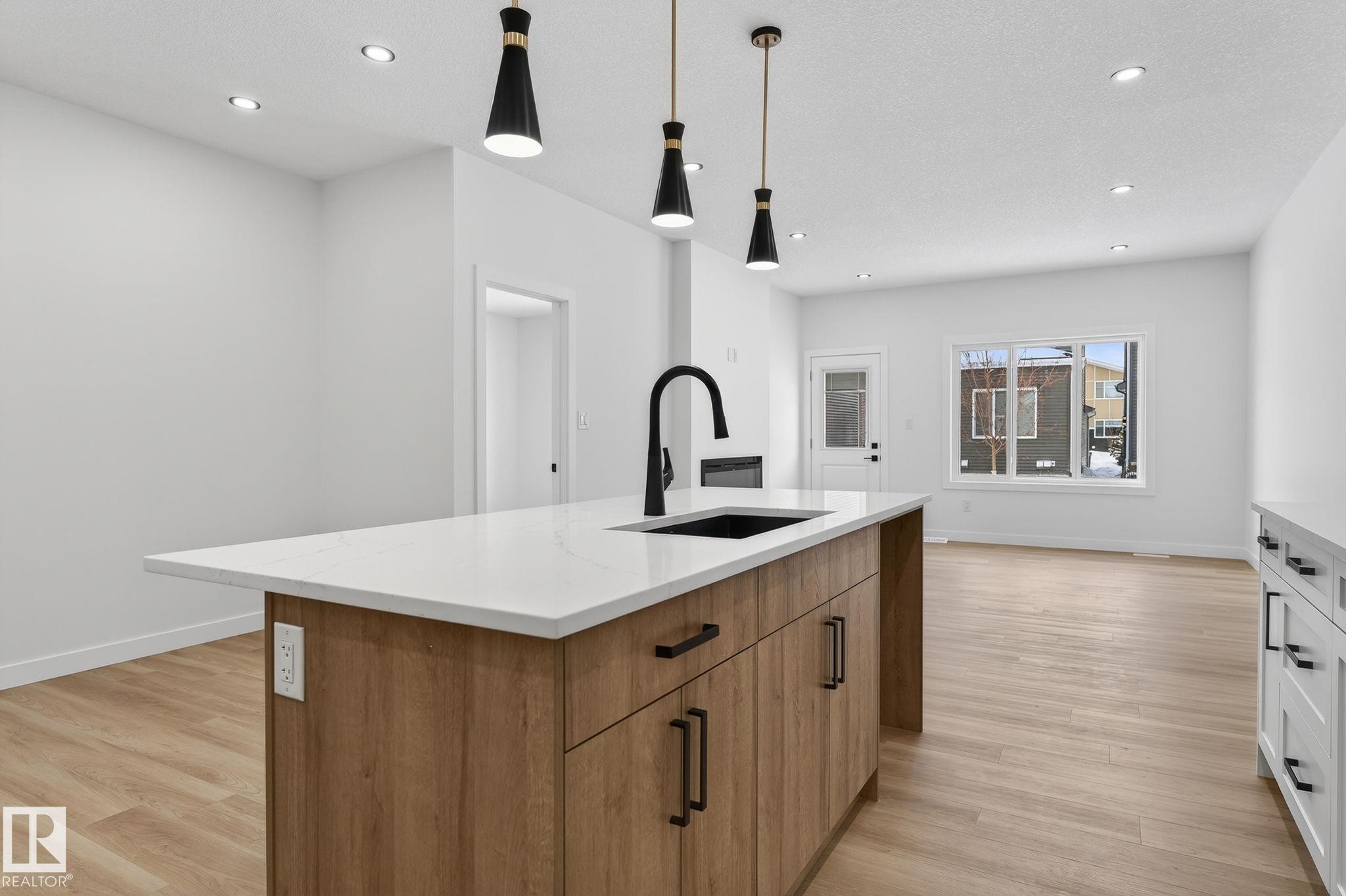 Kitchen featuring dual tone cabinetry, pendant lighting, a center island with sink, light stone counters, and light wood finished floors - 3318 Chickadee Drive, Edmonton, AB - Indoor Photo Showing Kitchen