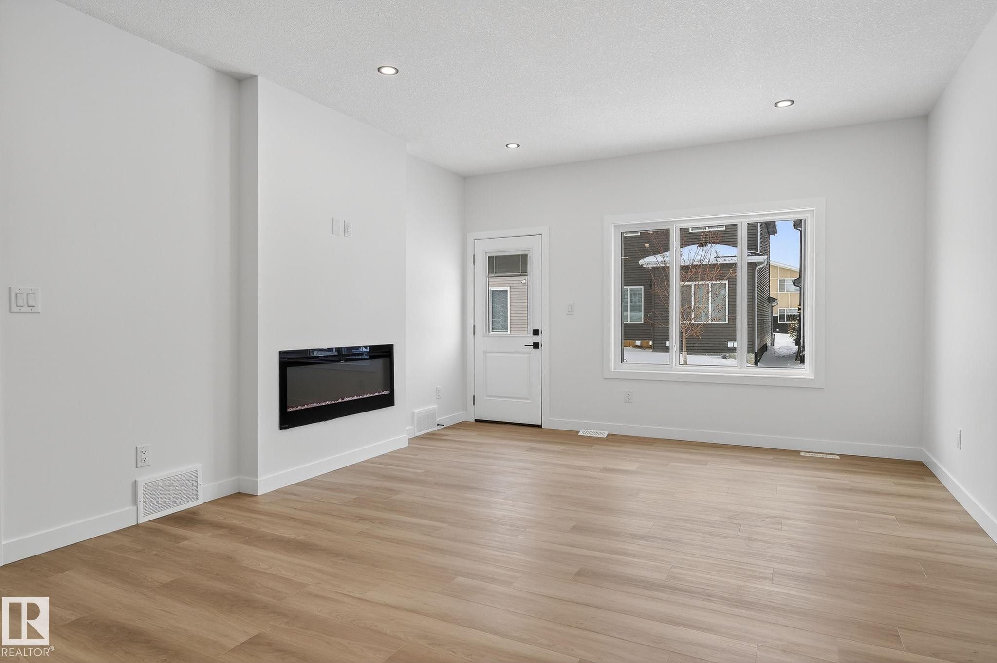 Unfurnished living room with light wood-style floors, a glass covered fireplace, and recessed lighting - 3318 Chickadee Drive, Edmonton, AB - Indoor Photo Showing Living Room With Fireplace