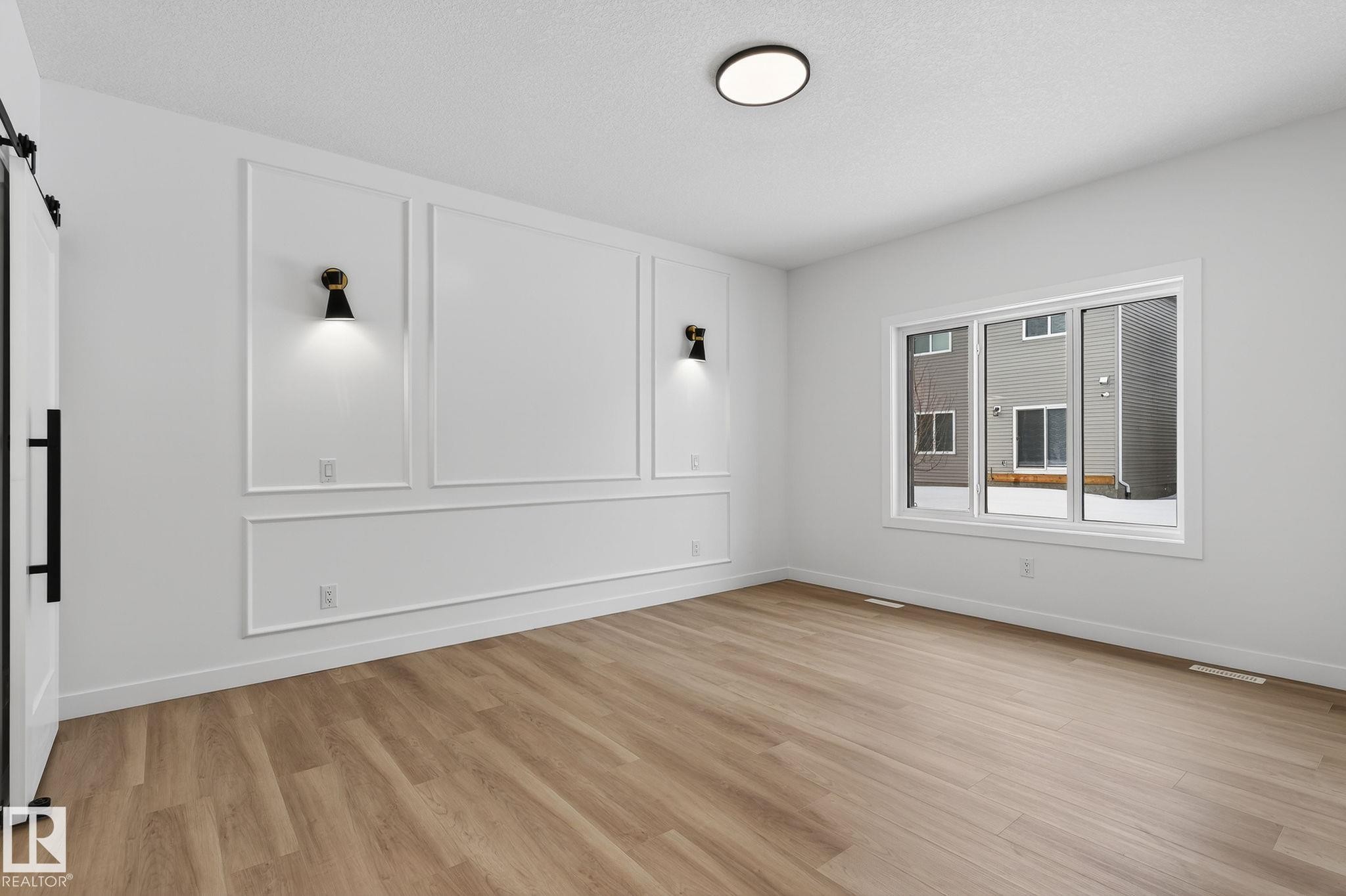 Spare room with light wood-type flooring, a barn door, a decorative wall, and a textured ceiling - 3318 Chickadee Drive, Edmonton, AB - Indoor Photo Showing Other Room