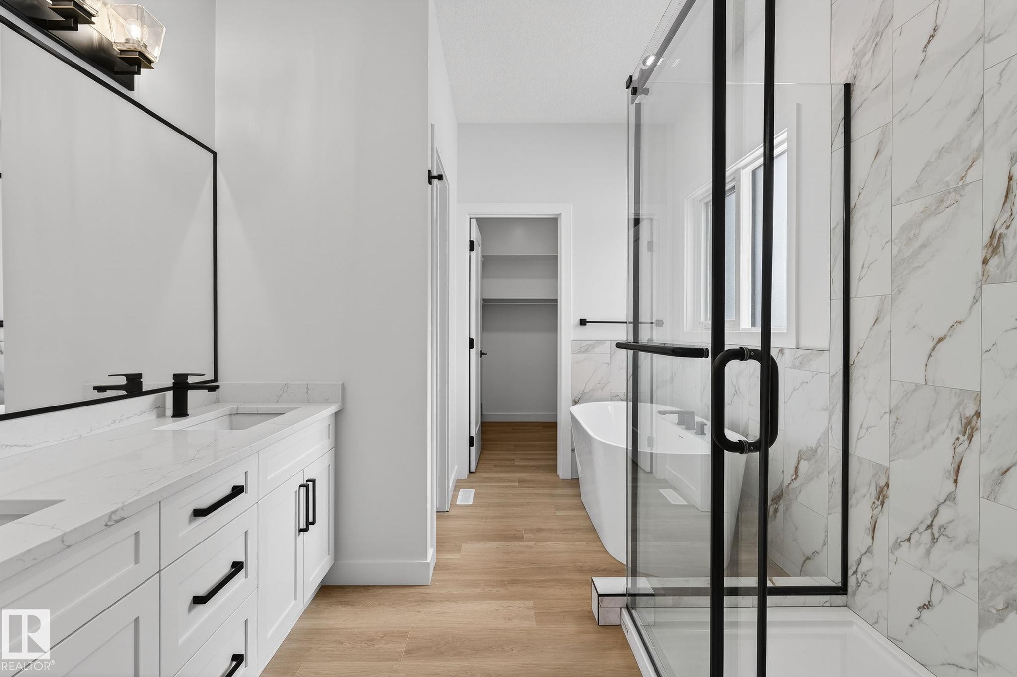 Bathroom featuring a marble finish shower, a freestanding tub, double vanity, a spacious closet, and light wood-type flooring - 3318 Chickadee Drive, Edmonton, AB - Indoor