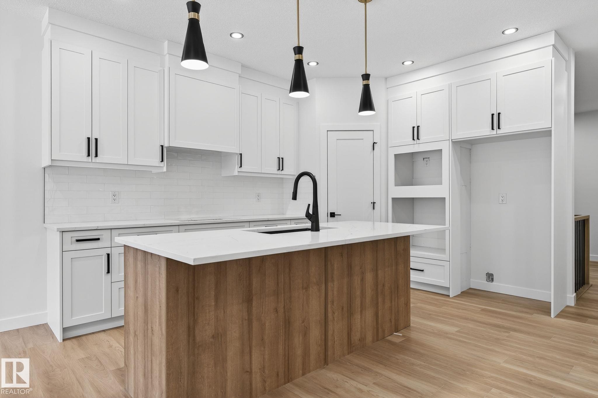 Dual tone kitchen featuring two tone cabinets, a kitchen island with sink, pendant lighting, light stone countertops, and light wood-type flooring - 3318 Chickadee Drive, Edmonton, AB - Indoor Photo Showing Kitchen With Upgraded Kitchen