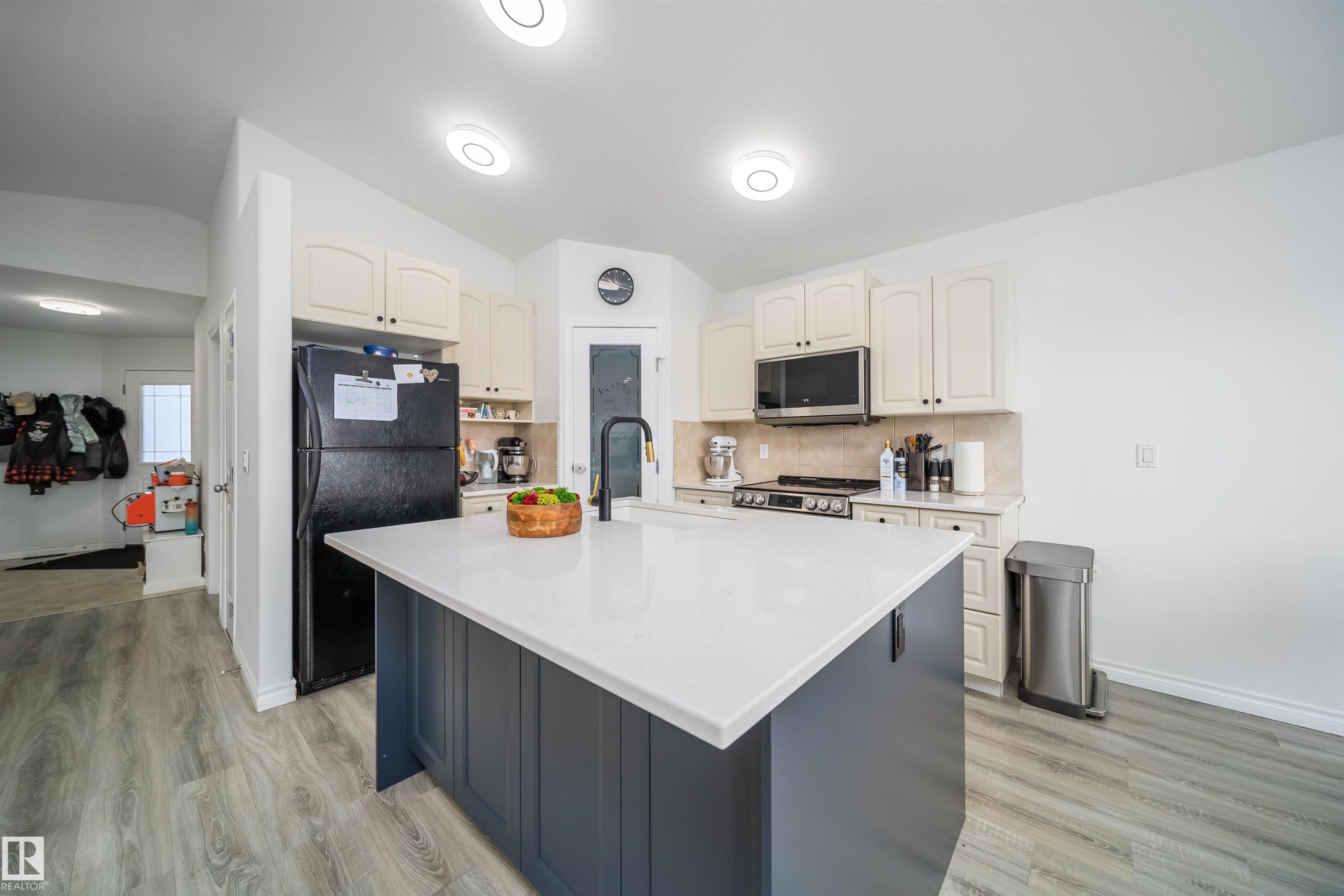 Two tone kitchen featuring stainless steel appliances, an island with sink, light wood-type flooring, tasteful backsplash, and dual tone cabinets - 1179 Oakland Drive, Devon, AB - Indoor Photo Showing Kitchen