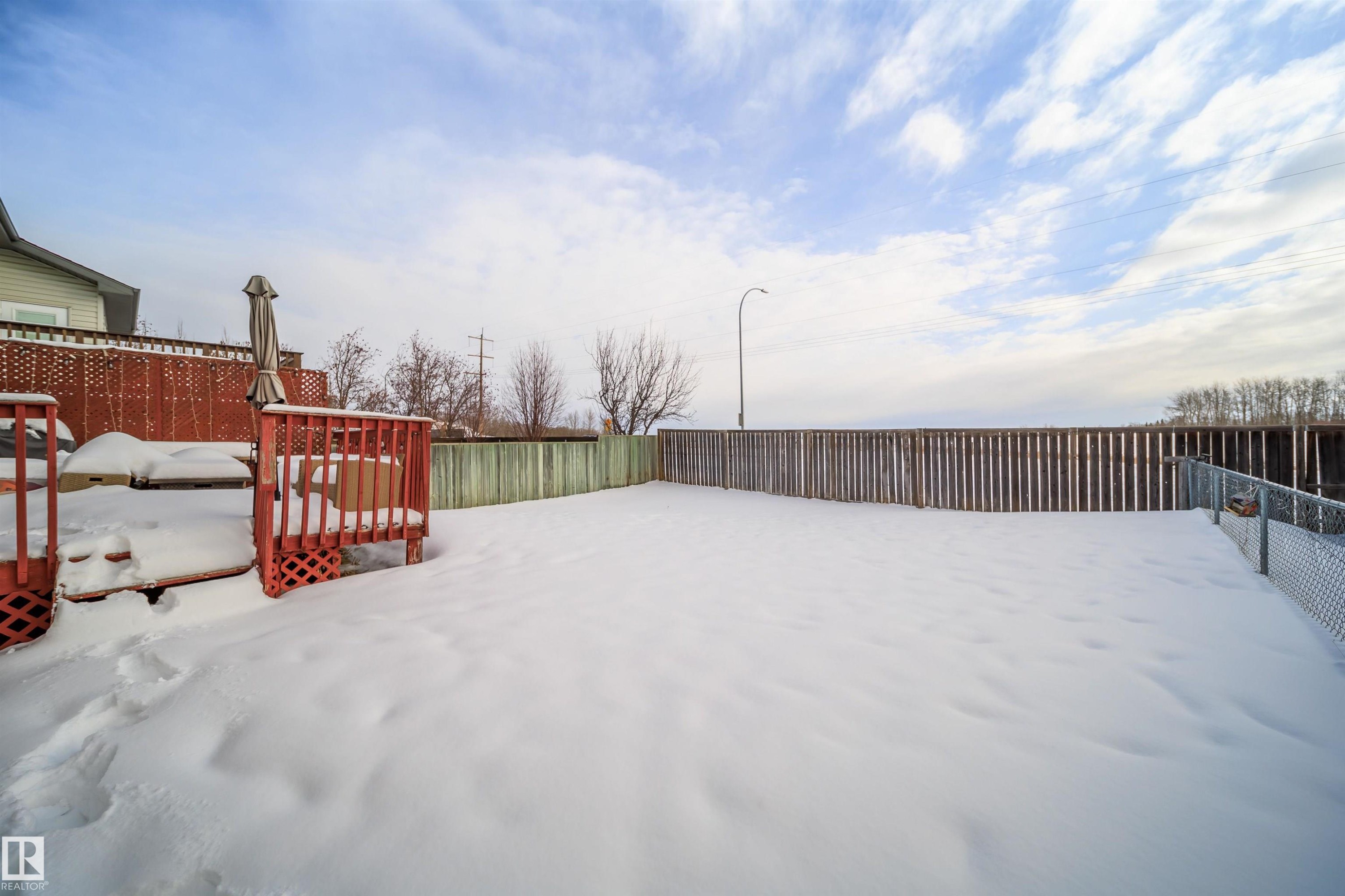 Yard covered in snow with a fenced backyard and a deck - 1179 Oakland Drive, Devon, AB - Outdoor