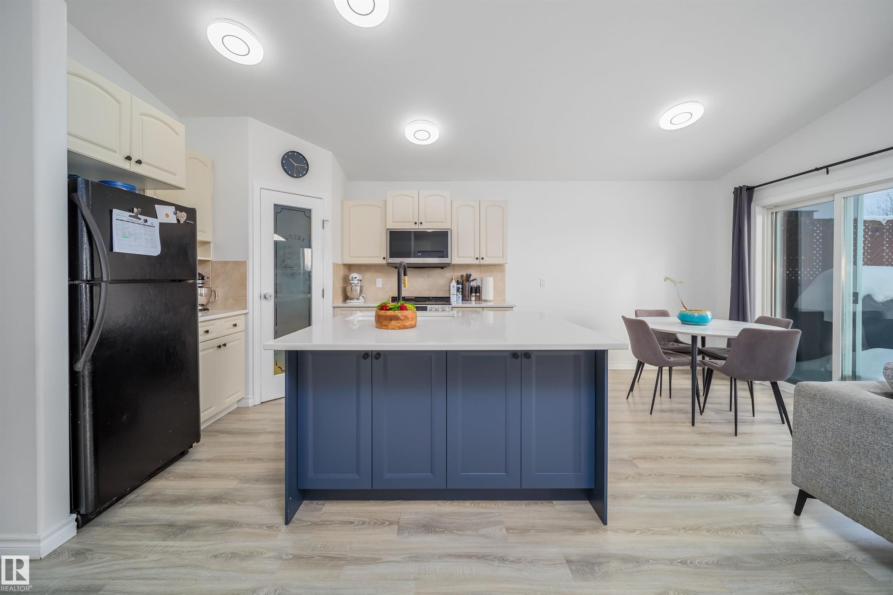 Kitchen featuring freestanding refrigerator, a center island with sink, two tone cabinetry, decorative backsplash, and light wood-style floors - 1179 Oakland Drive, Devon, AB - Indoor Photo Showing Kitchen