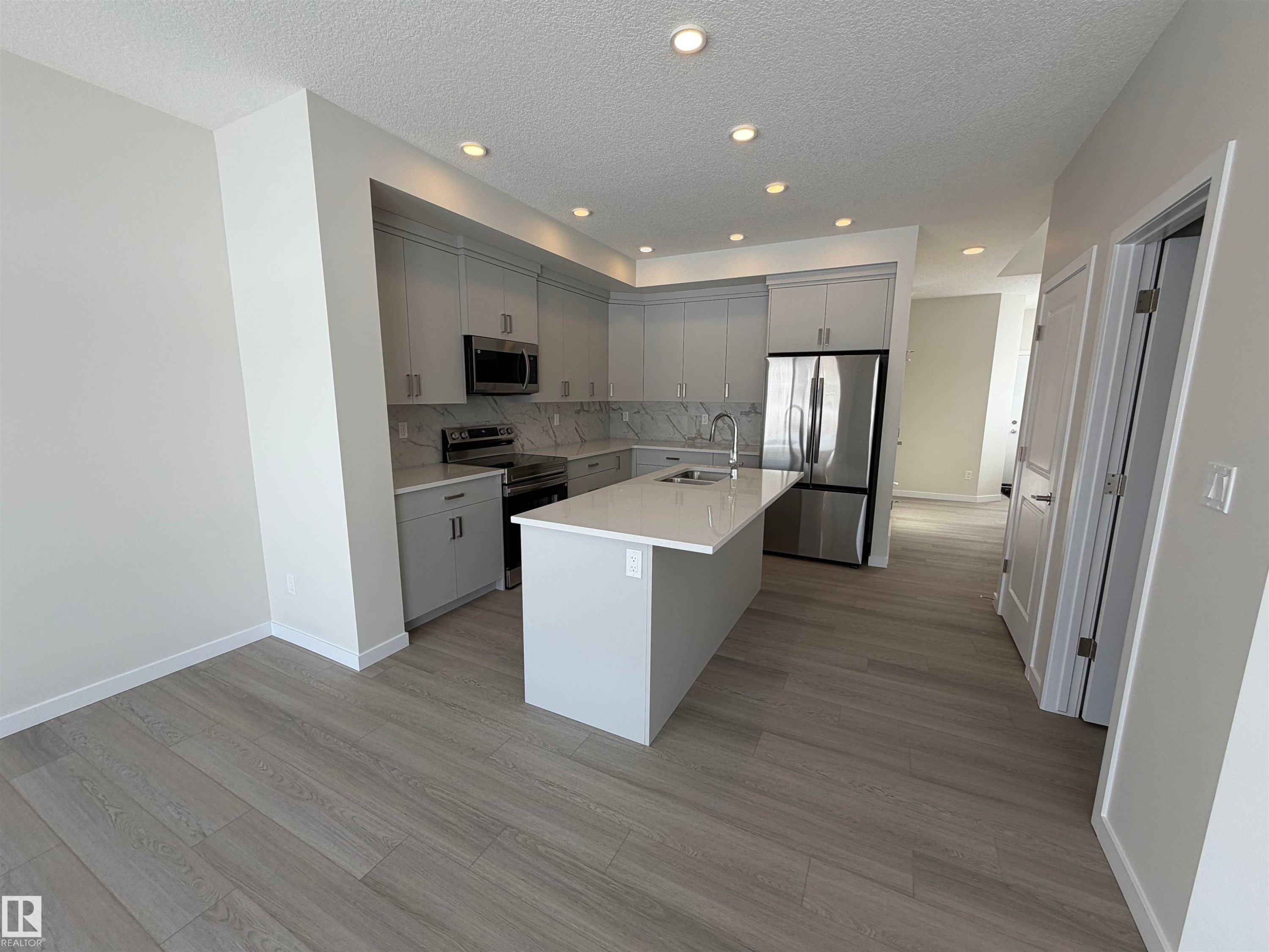 Kitchen featuring stainless steel appliances, an island with sink, gray cabinets, light wood-style floors, and a textured ceiling - 5756 Hawthorn Common, Edmonton, AB - Indoor Photo Showing Kitchen With Upgraded Kitchen