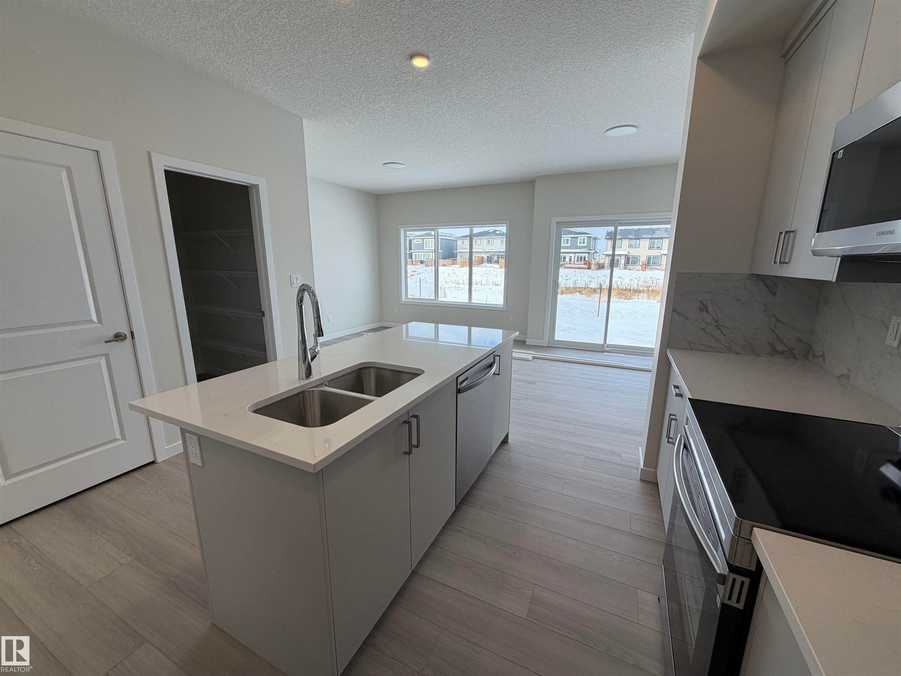 Kitchen with stainless steel appliances, a kitchen island with sink, light wood finished floors, white cabinets, and light stone countertops - 5756 Hawthorn Common, Edmonton, AB - Indoor Photo Showing Kitchen With Double Sink