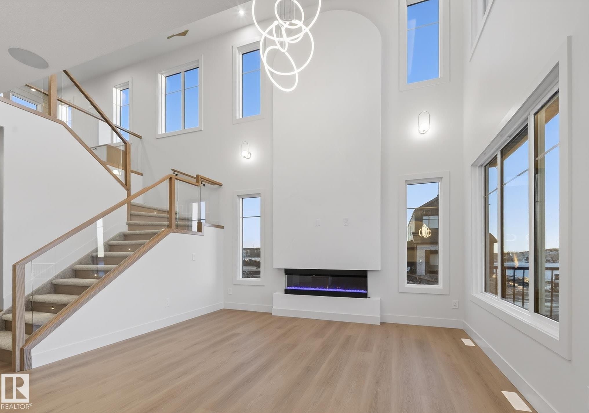 Unfurnished living room featuring light wood-style flooring, a chandelier, a glass covered fireplace, plenty of natural light, and a high ceiling - 4276 Charles Close, Edmonton, AB - Indoor Photo Showing Other Room