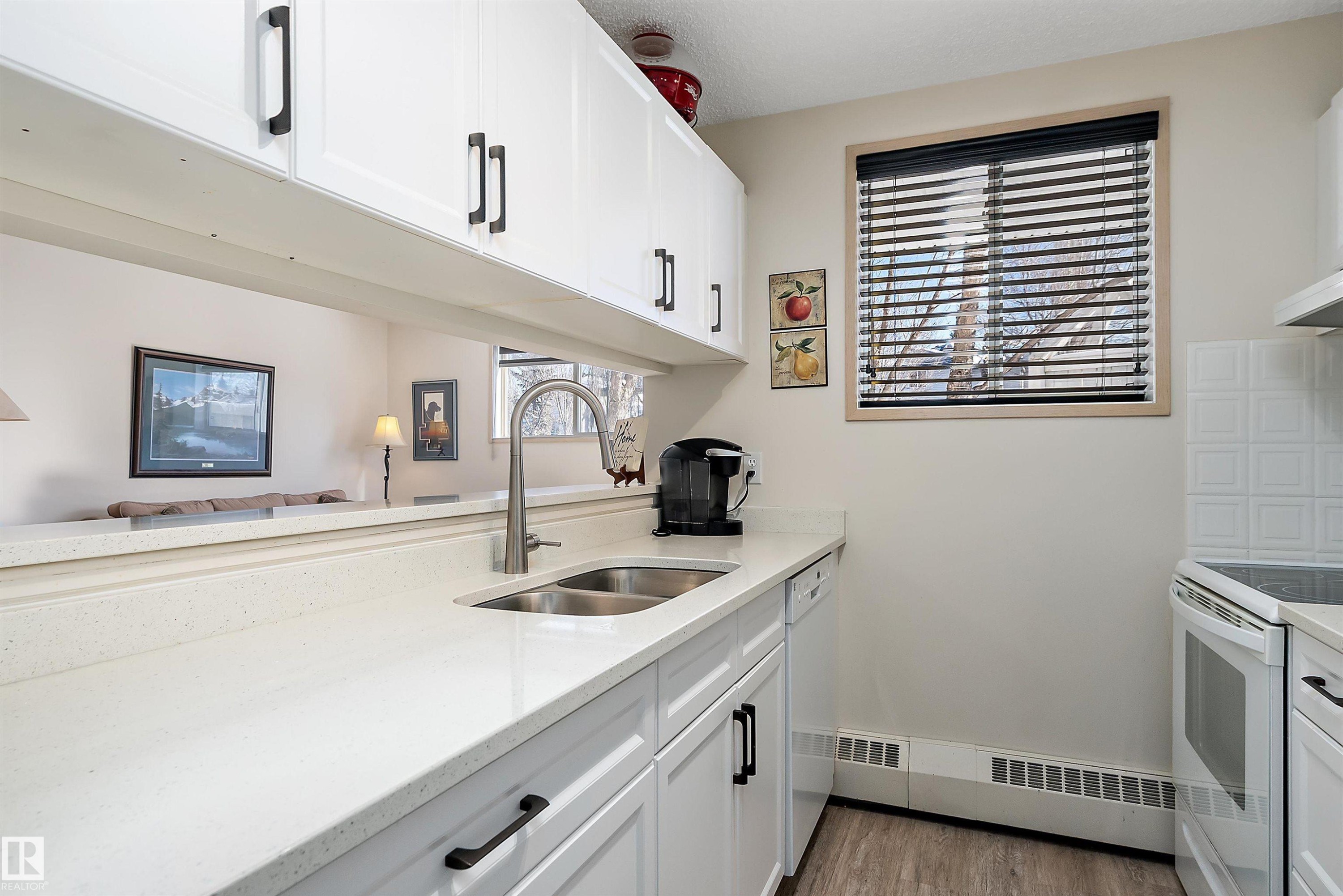 Kitchen featuring white cabinets, light stone countertops, light flooring, and white appliances - 116 11620 9A Avenue, Edmonton, AB - Indoor Photo Showing Kitchen With Double Sink