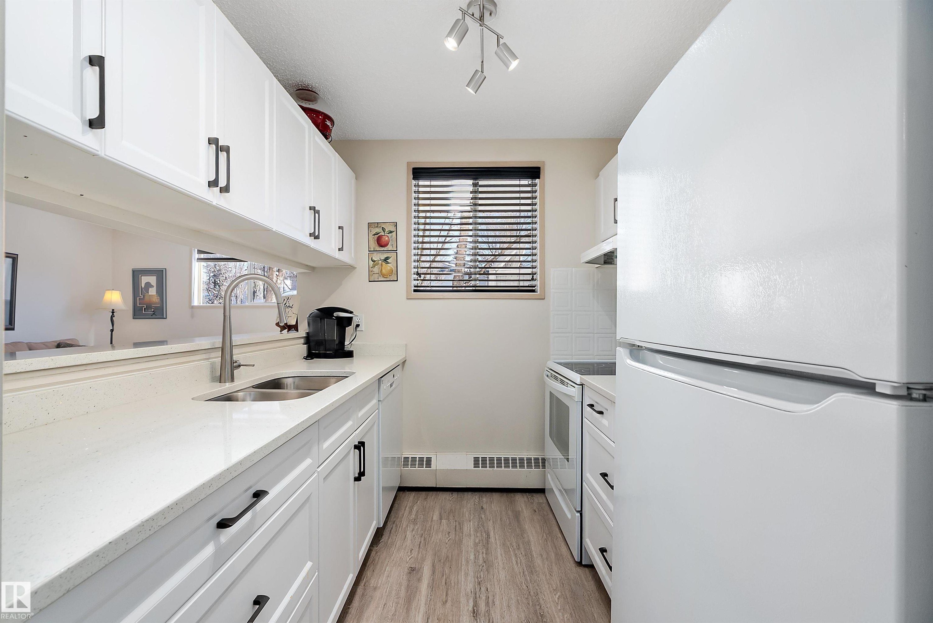Kitchen featuring white appliances, white cabinetry, light stone counters, and light floors - 116 11620 9A Avenue, Edmonton, AB - Indoor Photo Showing Kitchen With Double Sink
