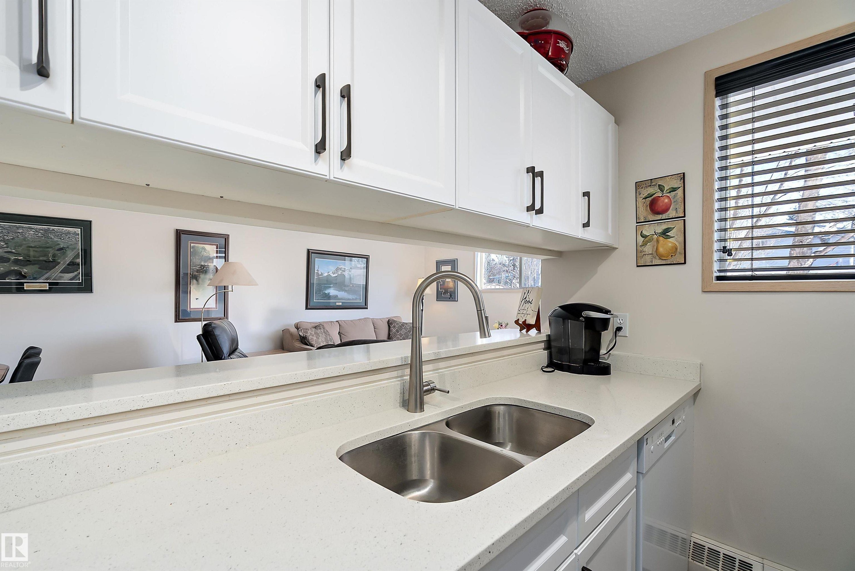 Kitchen with light stone countertops, white cabinetry, a textured ceiling, and white dishwasher - 116 11620 9A Avenue, Edmonton, AB - Indoor Photo Showing Kitchen With Double Sink
