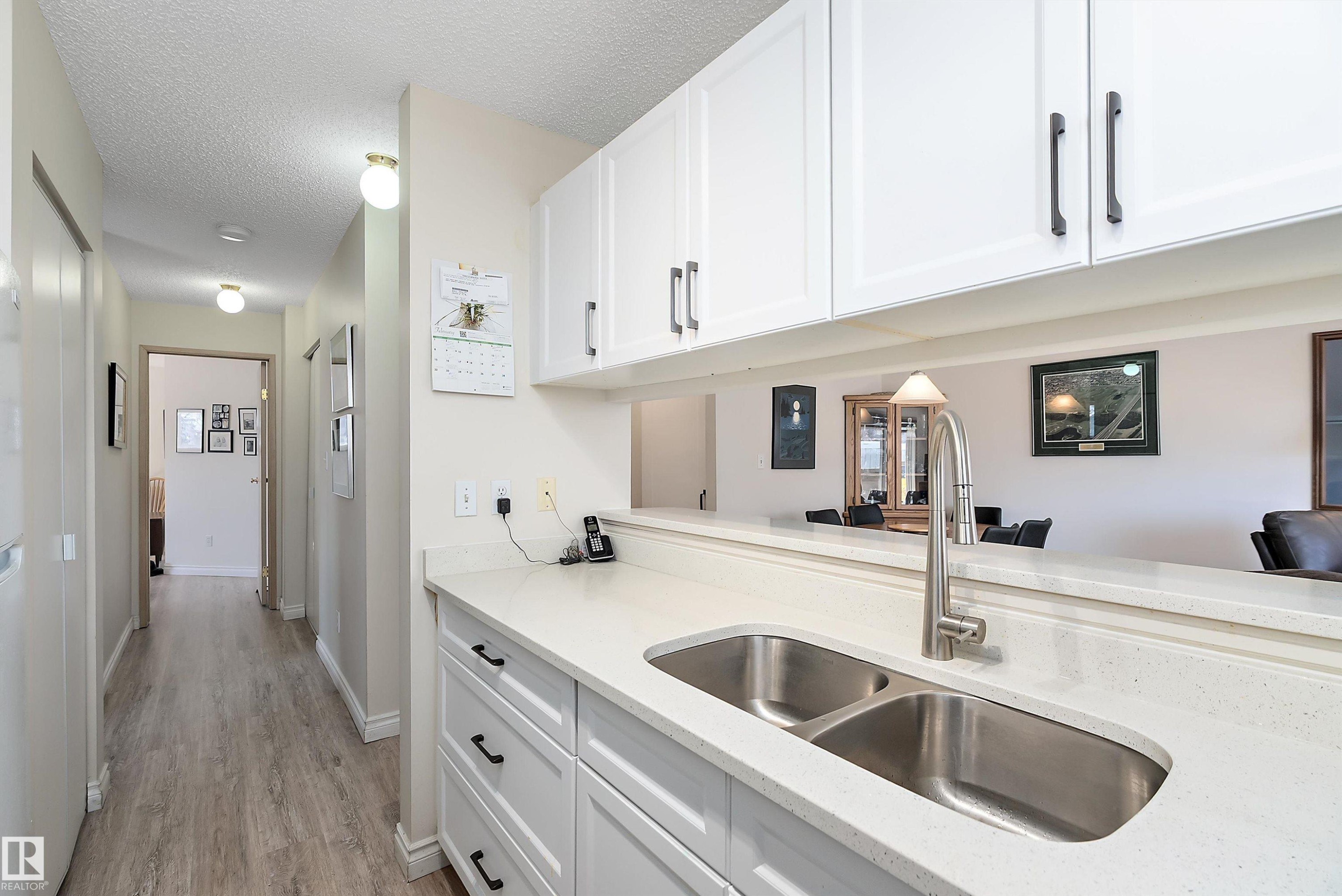 Kitchen featuring white cabinetry, a textured ceiling, light stone counters, and light flooring - 116 11620 9A Avenue, Edmonton, AB - Indoor Photo Showing Kitchen With Double Sink
