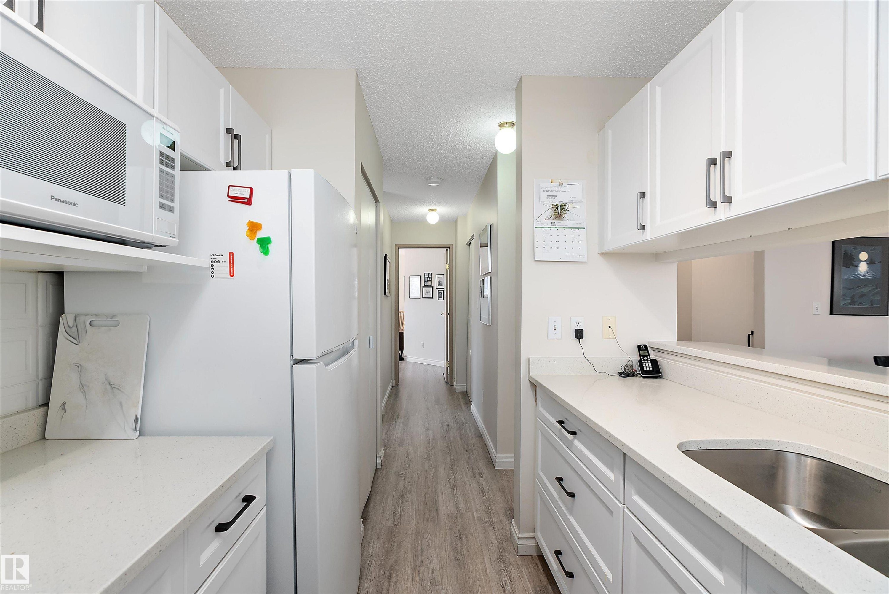 Kitchen featuring white appliances, white cabinets, light stone counters, a textured ceiling, and light wood-style flooring - 116 11620 9A Avenue, Edmonton, AB - Indoor Photo Showing Kitchen