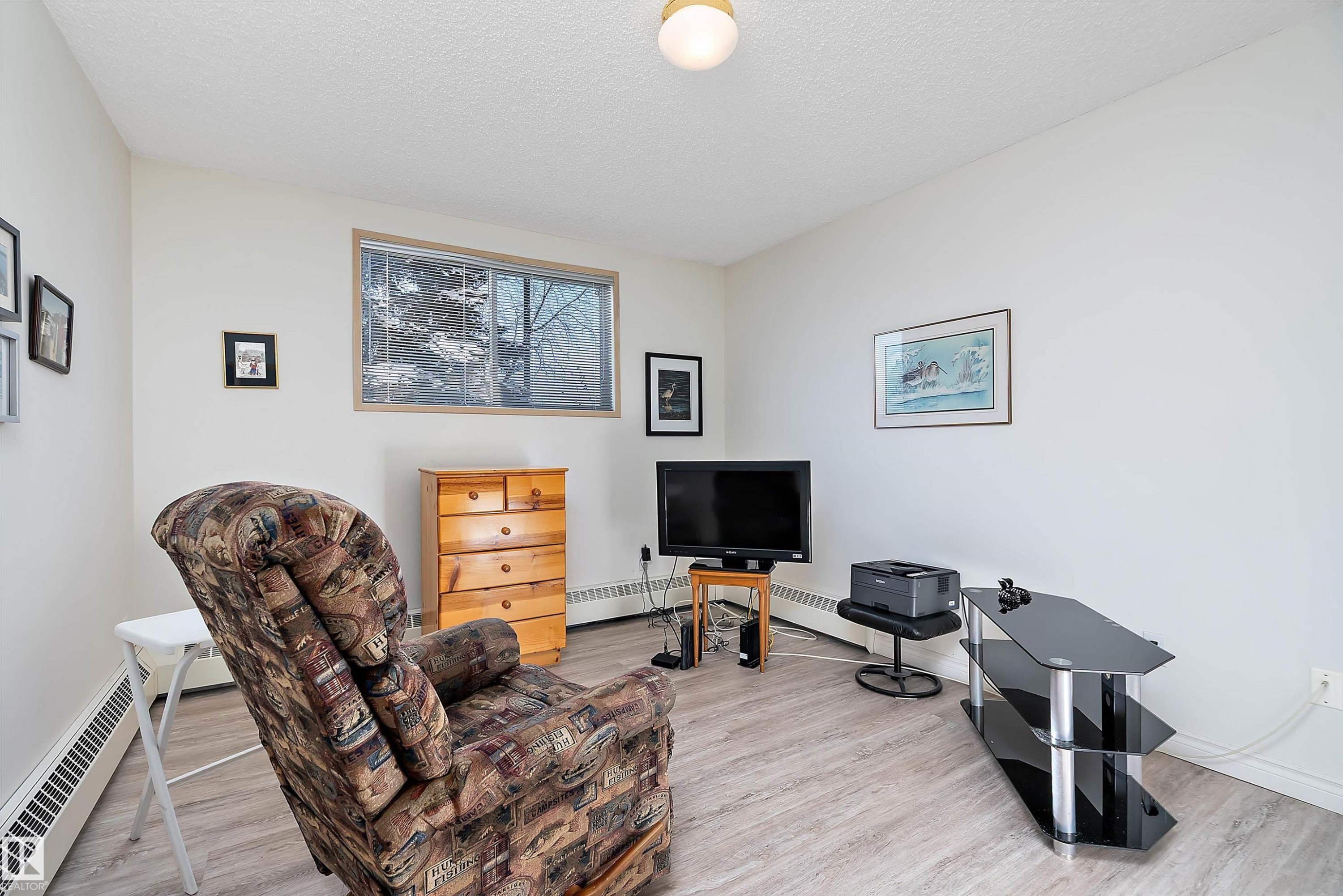 Living area featuring a textured ceiling, baseboard heating, and light floors - 116 11620 9A Avenue, Edmonton, AB - Indoor