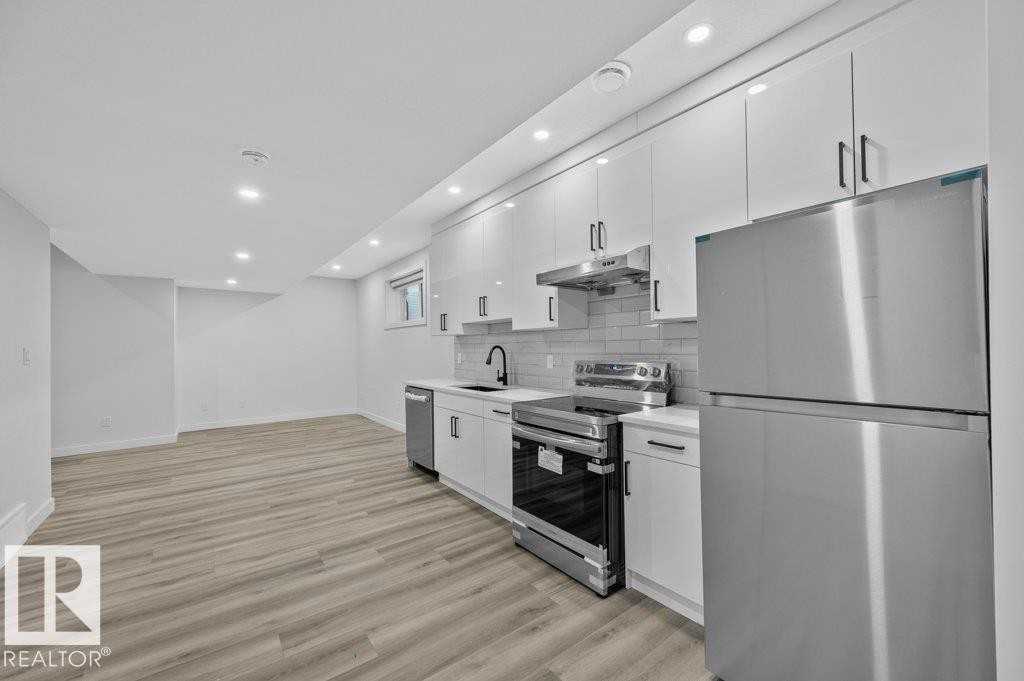 Kitchen featuring stainless steel appliances, recessed lighting, white cabinetry, light wood finished floors, and tasteful backsplash - Edmonton, AB - Indoor Photo Showing Kitchen