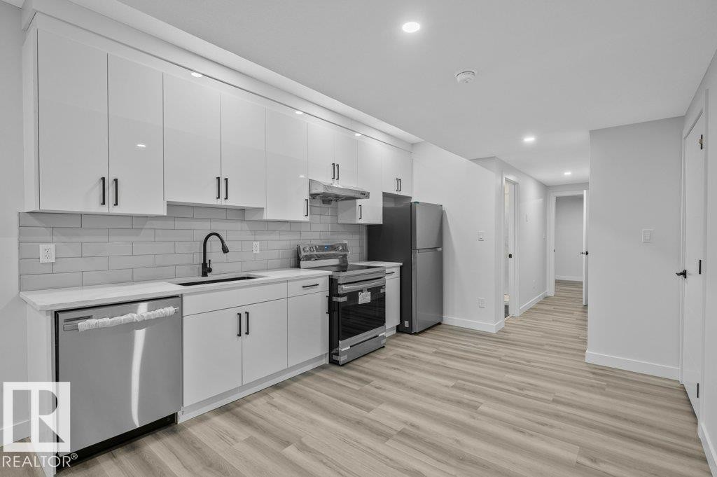 Kitchen featuring stainless steel appliances, white cabinetry, light wood finished floors, recessed lighting, and backsplash - Edmonton, AB - Indoor Photo Showing Kitchen