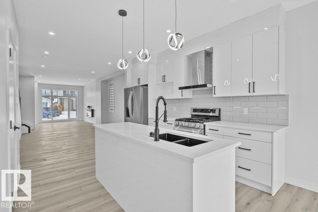Kitchen featuring an island with sink, white cabinetry, stainless steel appliances, tasteful backsplash, and open floor plan - Edmonton, AB - Indoor Photo Showing Kitchen With Double Sink With Upgraded Kitchen