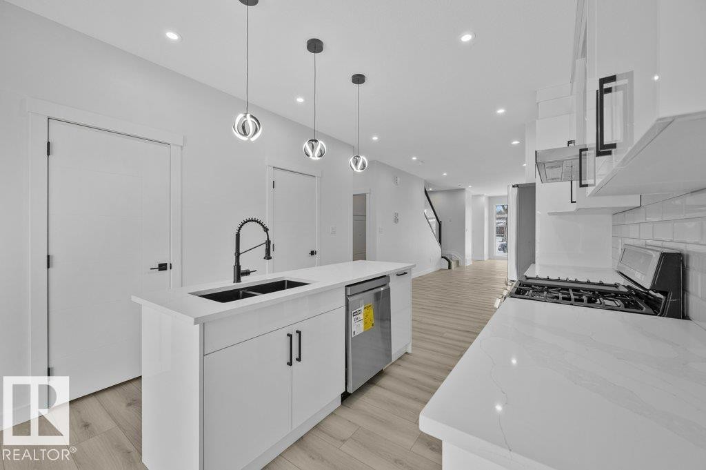 Kitchen featuring an island with sink, light stone counters, white cabinetry, stainless steel appliances, and pendant lighting - Edmonton, AB - Indoor Photo Showing Kitchen With Double Sink