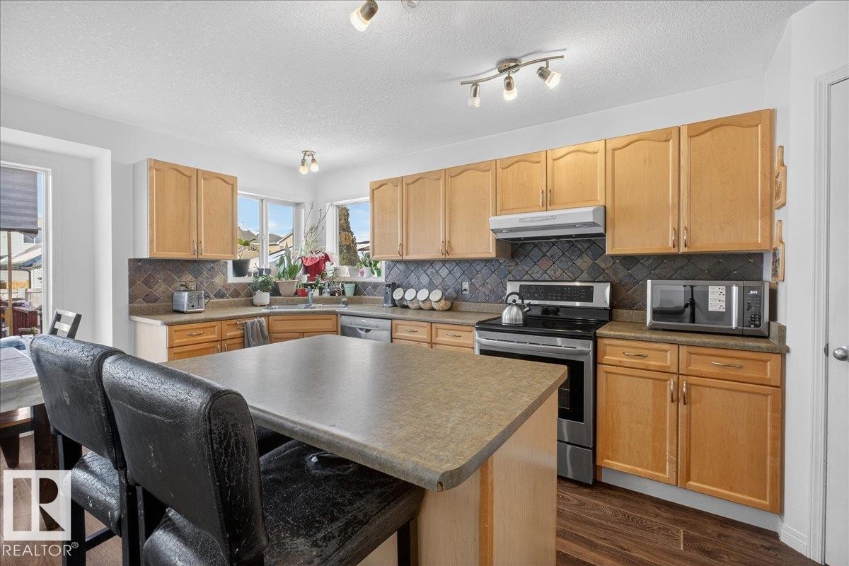Kitchen featuring stainless steel appliances, light wood finish cabinets, dark wood-style flooring, a center island, and a kitchen bar - 4519 Turner Square, Edmonton, AB - Indoor Photo Showing Kitchen With Double Sink