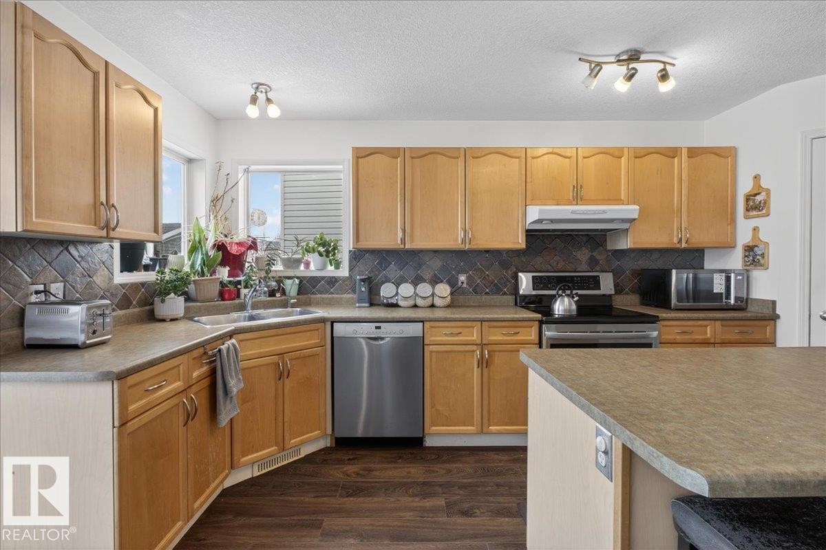 Kitchen with stainless steel appliances, dark wood-style floors, light countertops, light wood finish cabinets, and a textured ceiling - 4519 Turner Square, Edmonton, AB - Indoor Photo Showing Kitchen With Double Sink