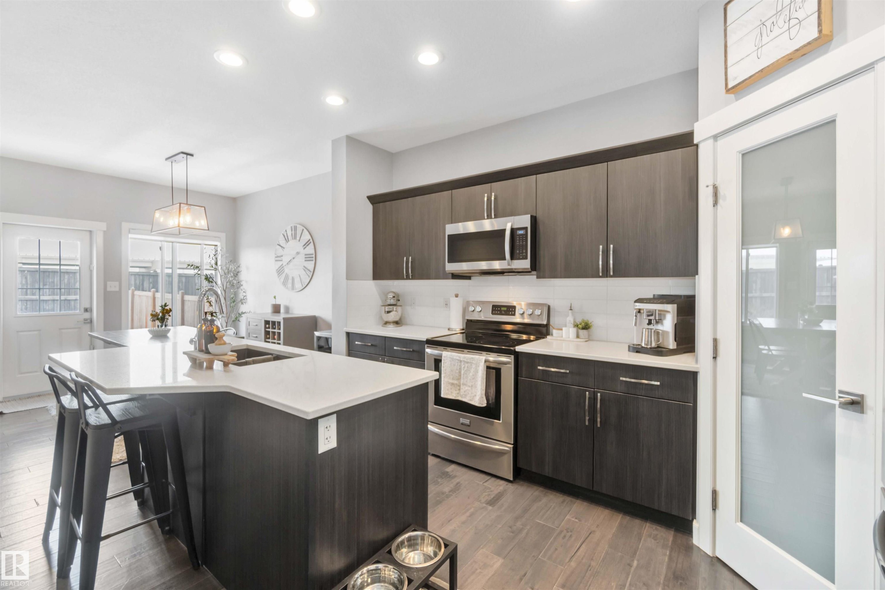 Kitchen with stainless steel appliances, dark wood finish cabinets, a center island with sink, dark wood finished floors, and pendant lighting - 17143 38 Street, Edmonton, AB - Indoor Photo Showing Kitchen With Double Sink With Upgraded Kitchen