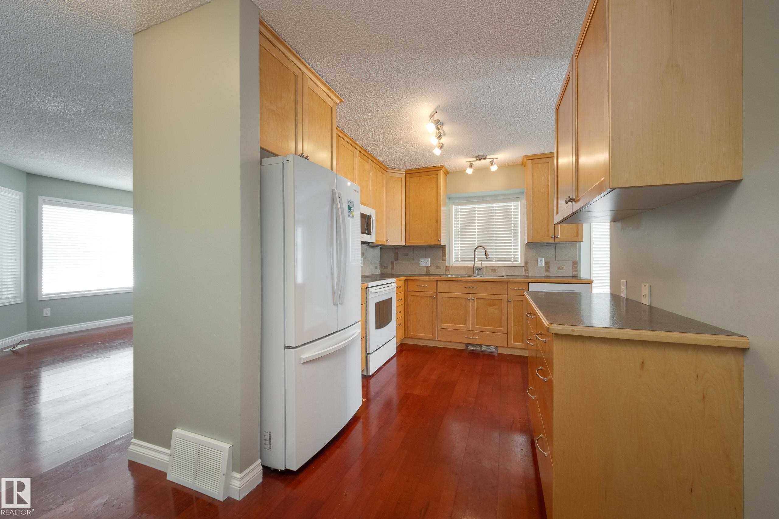 Kitchen featuring white appliances, light wood finish cabinets, dark wood finished floors, a textured ceiling, and tasteful backsplash - 9916 178 Avenue, Edmonton, AB - Indoor Photo Showing Kitchen