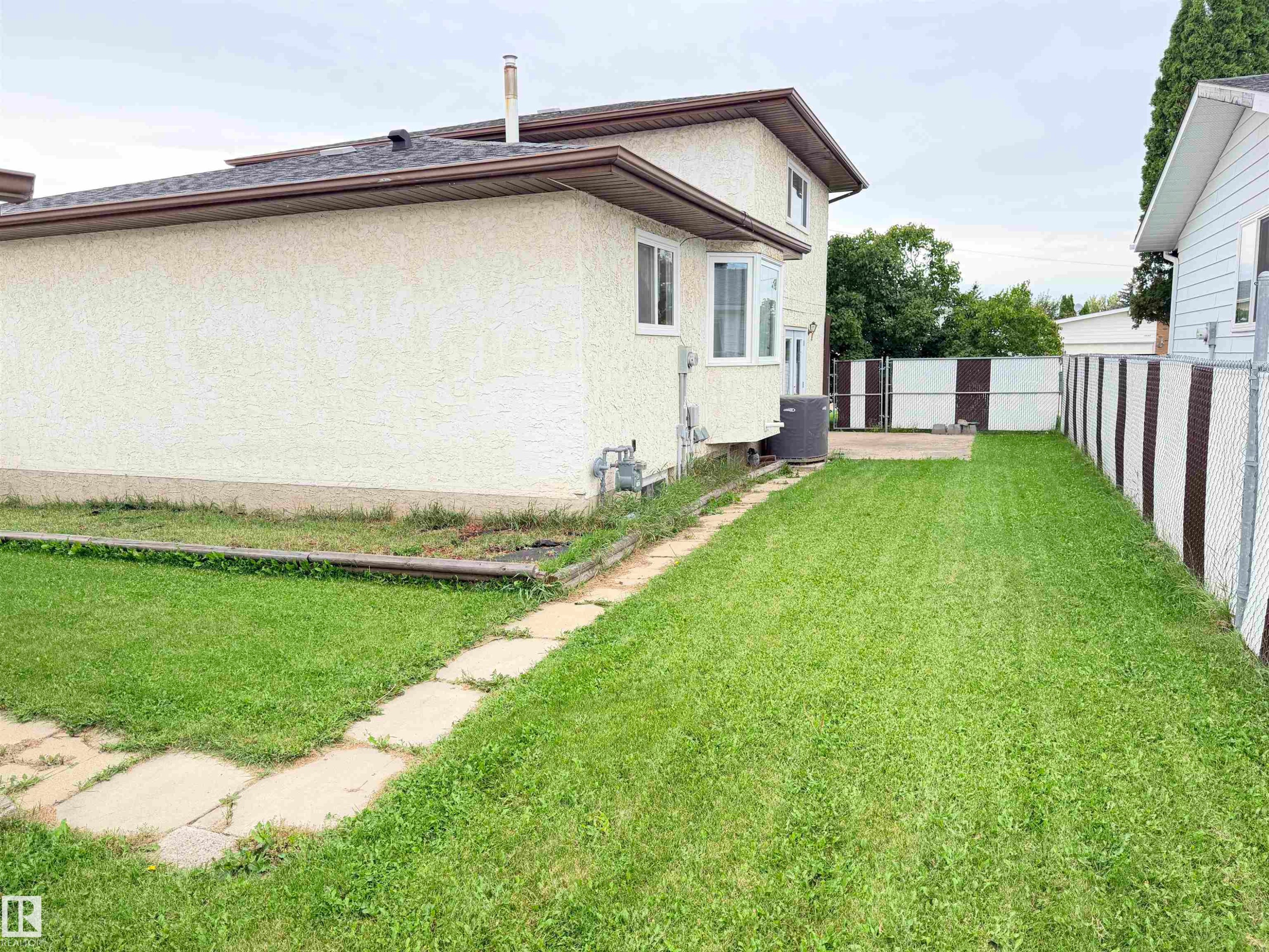 Expansive side yard featuring a manicured lawn, concrete paver pathway, and chain-link fencing - 10503 110 Street, Westlock, AB