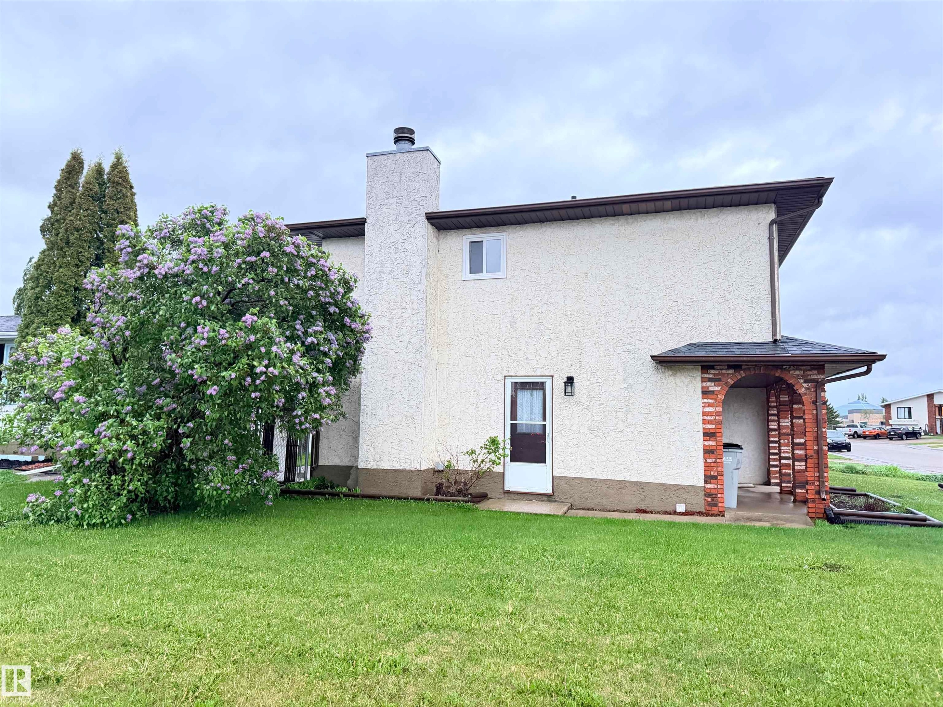 Stucco exterior with a prominent chimney and a mature flowering tree - 10503 110 Street, Westlock, AB