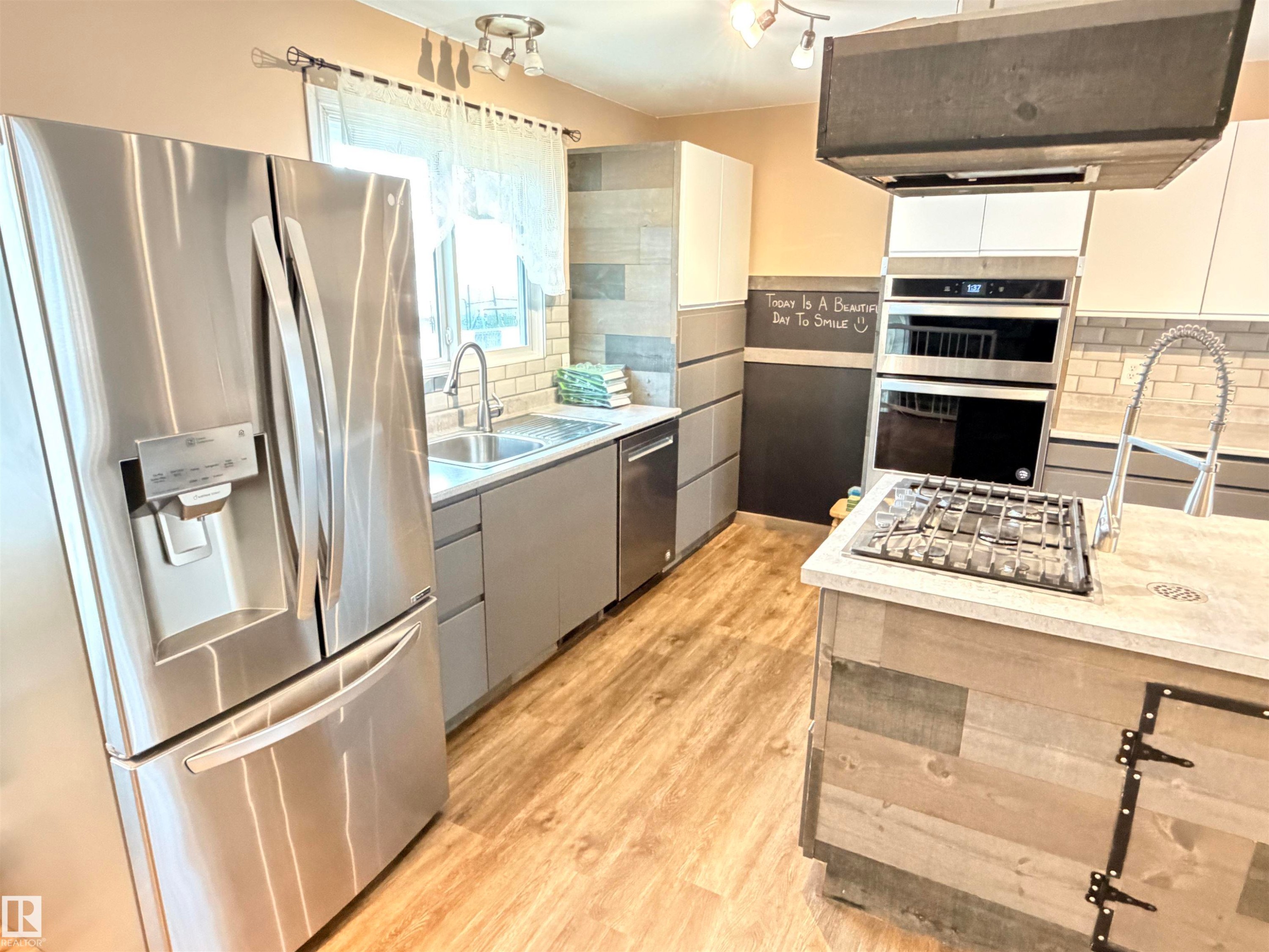 Stainless steel French door refrigerator, wood-finish flooring, undermount sink, built-in double oven, and gas cooktop - 10503 110 Street, Westlock, AB