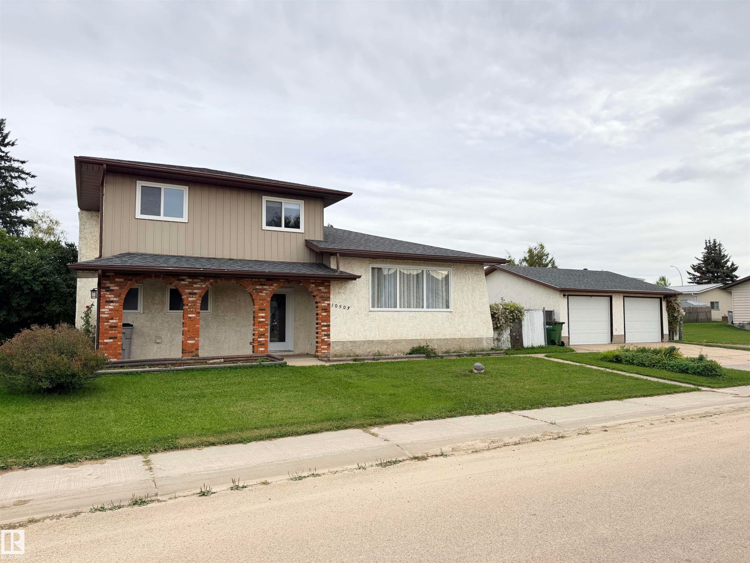 Two-story residence with brick archway detailing, a light-colored stucco finish, and a two-car garage with white doors - 10503 110 Street, Westlock, AB