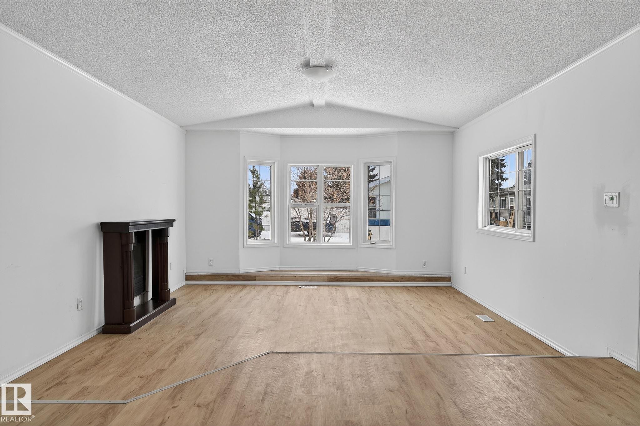 Unfurnished living room with a fireplace with raised hearth, healthy amount of natural light, light wood-style flooring, and a textured ceiling - 72 Evergreen Park, Edmonton, AB - Indoor Photo Showing Other Room
