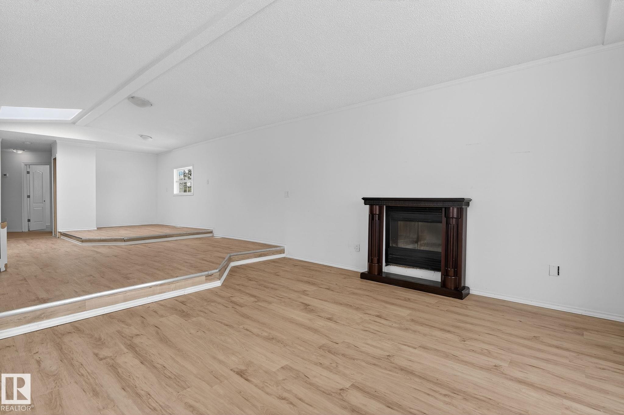 Unfurnished living room featuring a glass covered fireplace, light wood finished floors, and a skylight - 72 Evergreen Park, Edmonton, AB - Indoor With Fireplace
