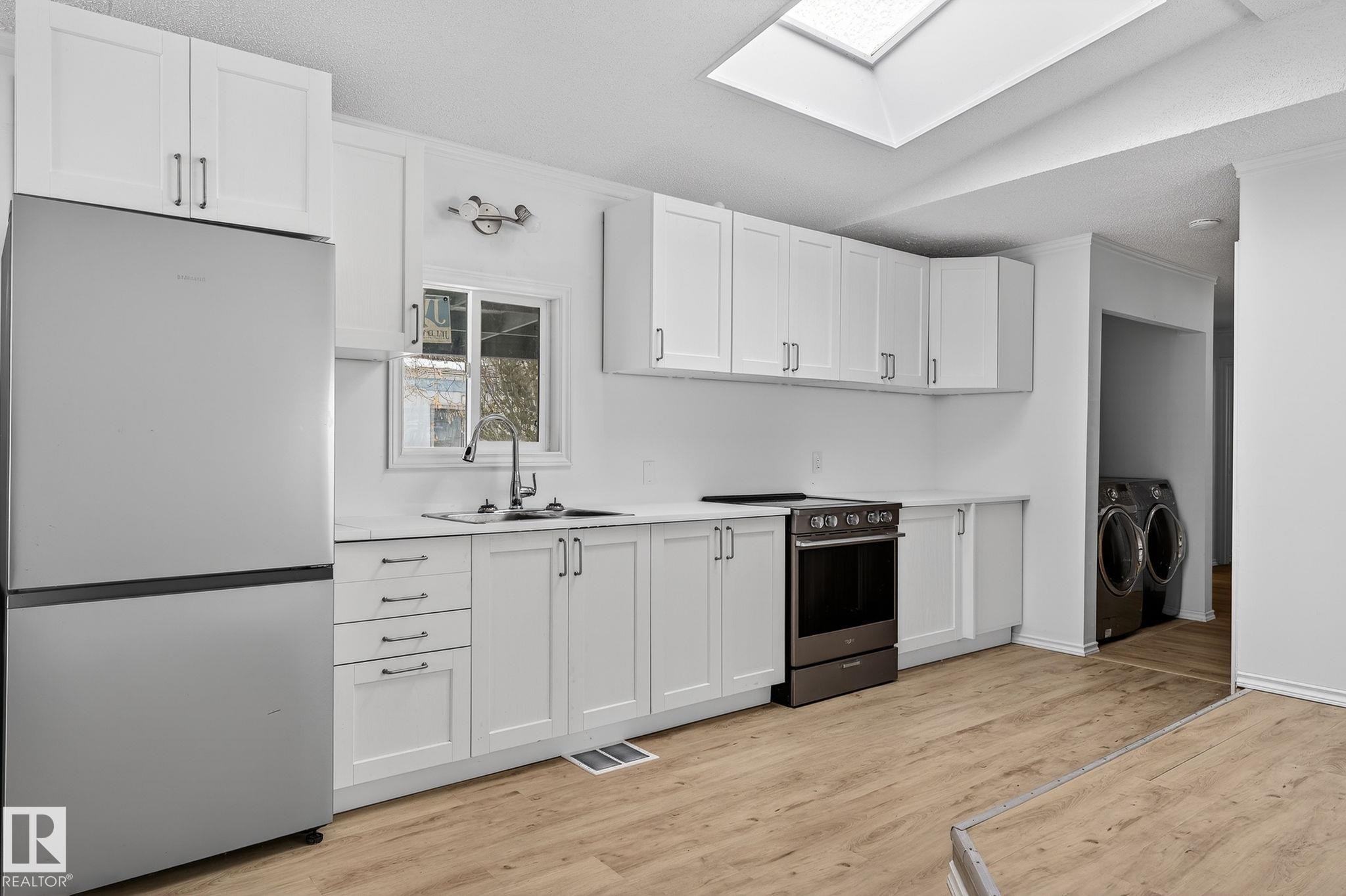 Kitchen with stainless steel appliances, white cabinets, a skylight, light wood-type flooring, and vaulted ceiling - 72 Evergreen Park, Edmonton, AB - Indoor Photo Showing Kitchen With Double Sink