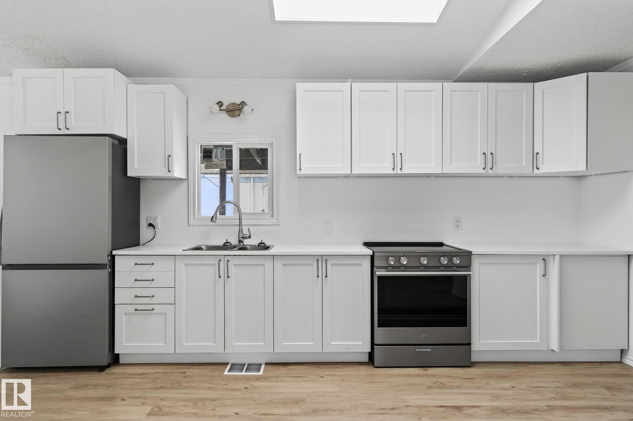Kitchen featuring stainless steel appliances, a skylight, white cabinetry, and light wood finished floors - 72 Evergreen Park, Edmonton, AB - Indoor Photo Showing Kitchen With Double Sink