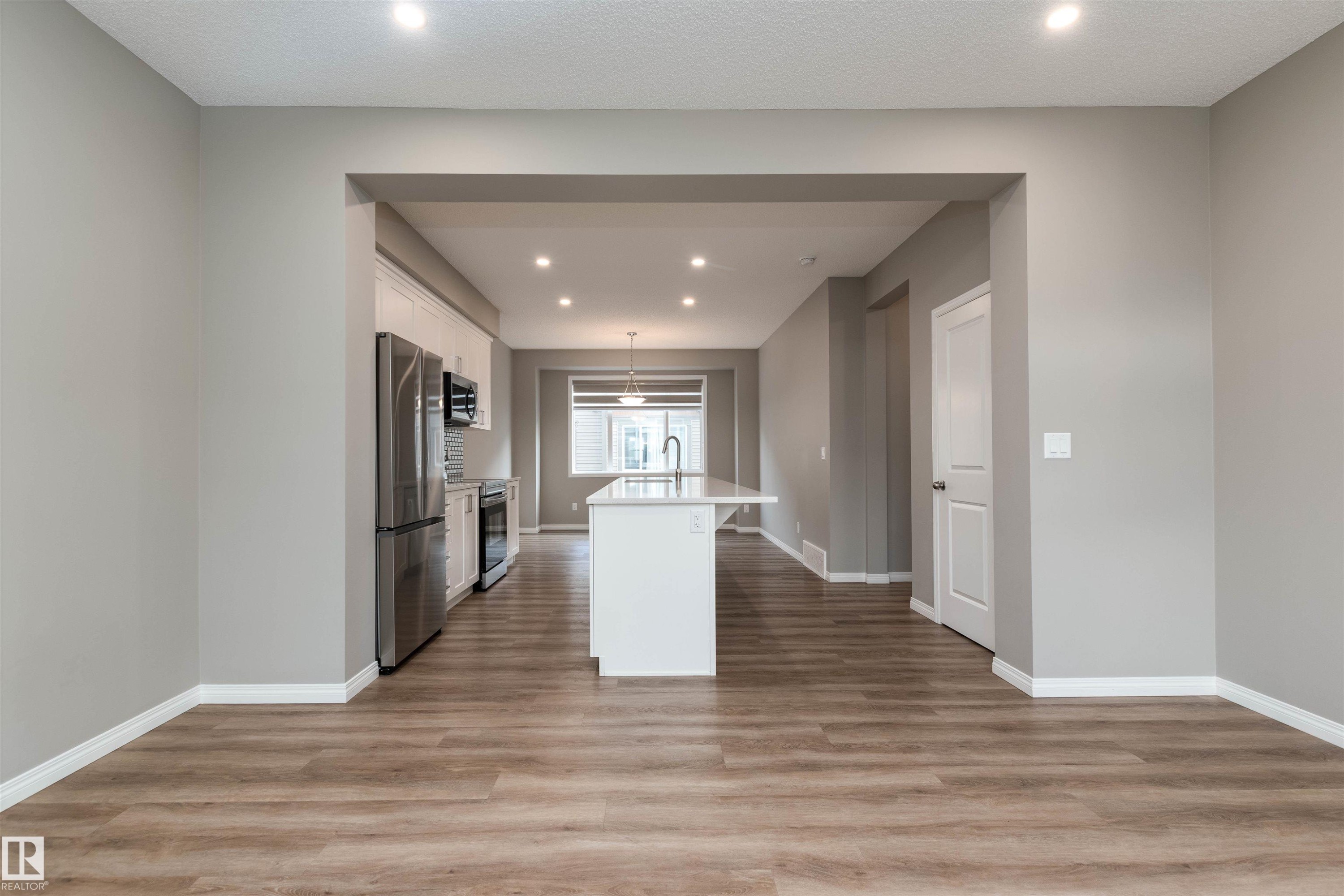 Kitchen with a center island with sink, white cabinets, recessed lighting, decorative light fixtures, and light wood-type flooring - 105 2072 Wonnacott Way, Edmonton, AB - Indoor Photo Showing Other Room
