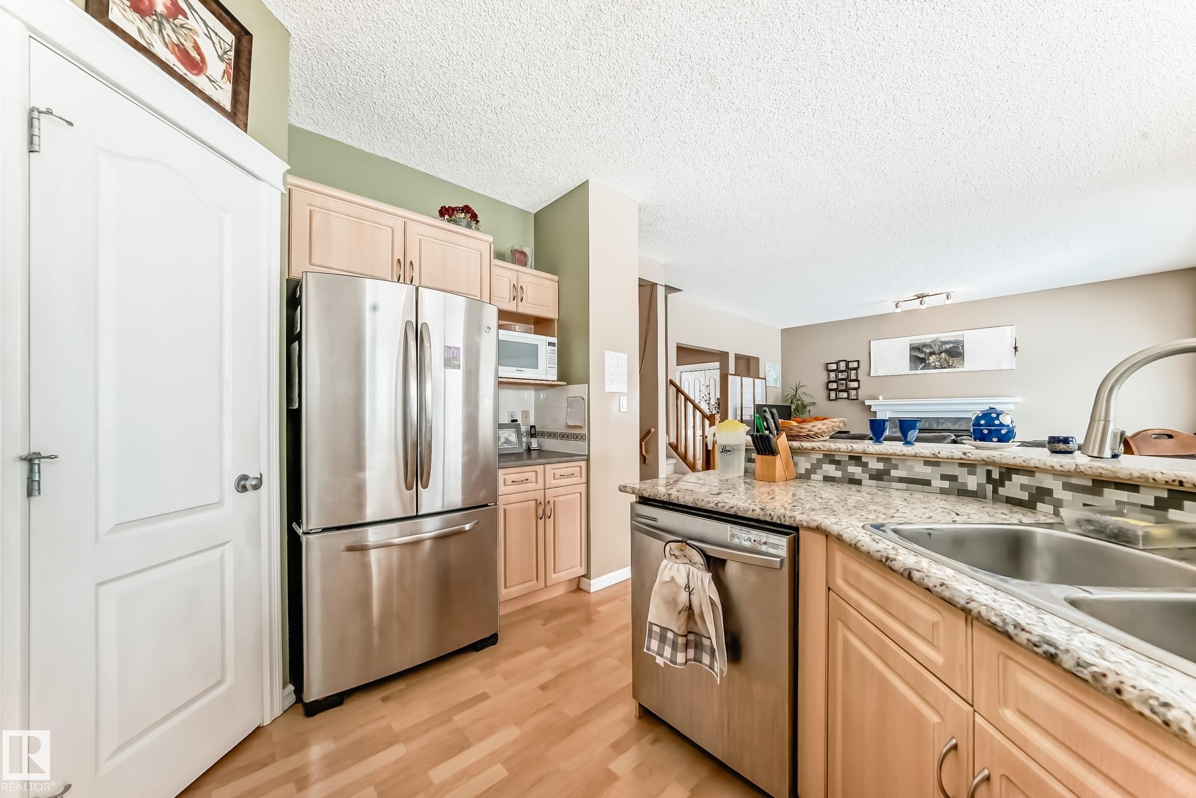 Kitchen featuring light wood finish cabinets, stainless steel appliances, decorative backsplash, light stone countertops, and light wood-style floors - 4619 151 Avenue, Edmonton, AB - Indoor Photo Showing Kitchen With Stainless Steel Kitchen With Double Sink