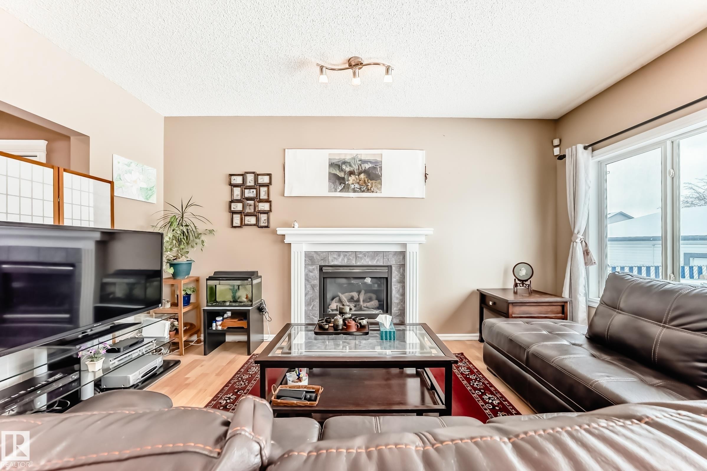 Living room with a tile fireplace, light wood finished floors, and a textured ceiling - 4619 151 Avenue, Edmonton, AB - Indoor Photo Showing Living Room With Fireplace