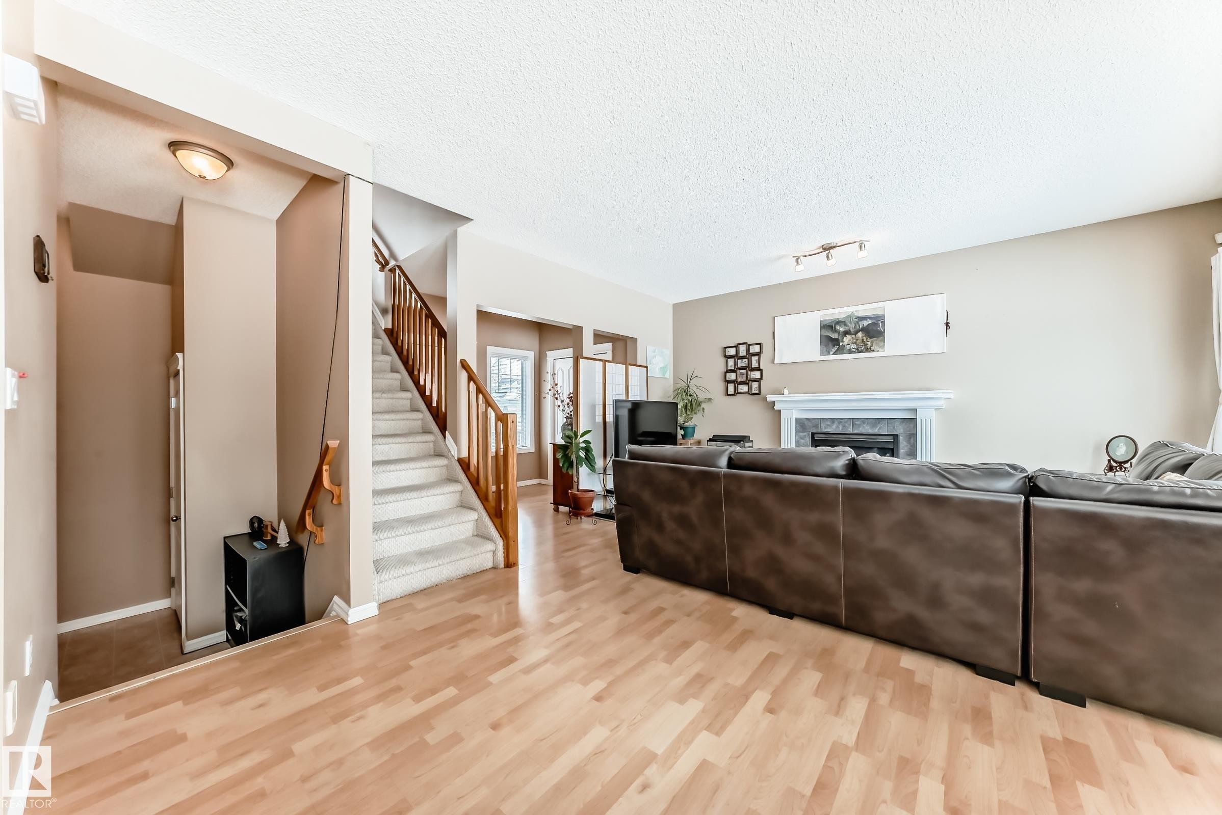 Living room featuring light wood finished floors, a fireplace, a textured ceiling, and track lighting - 4619 151 Avenue, Edmonton, AB - Indoor Photo Showing Living Room With Fireplace