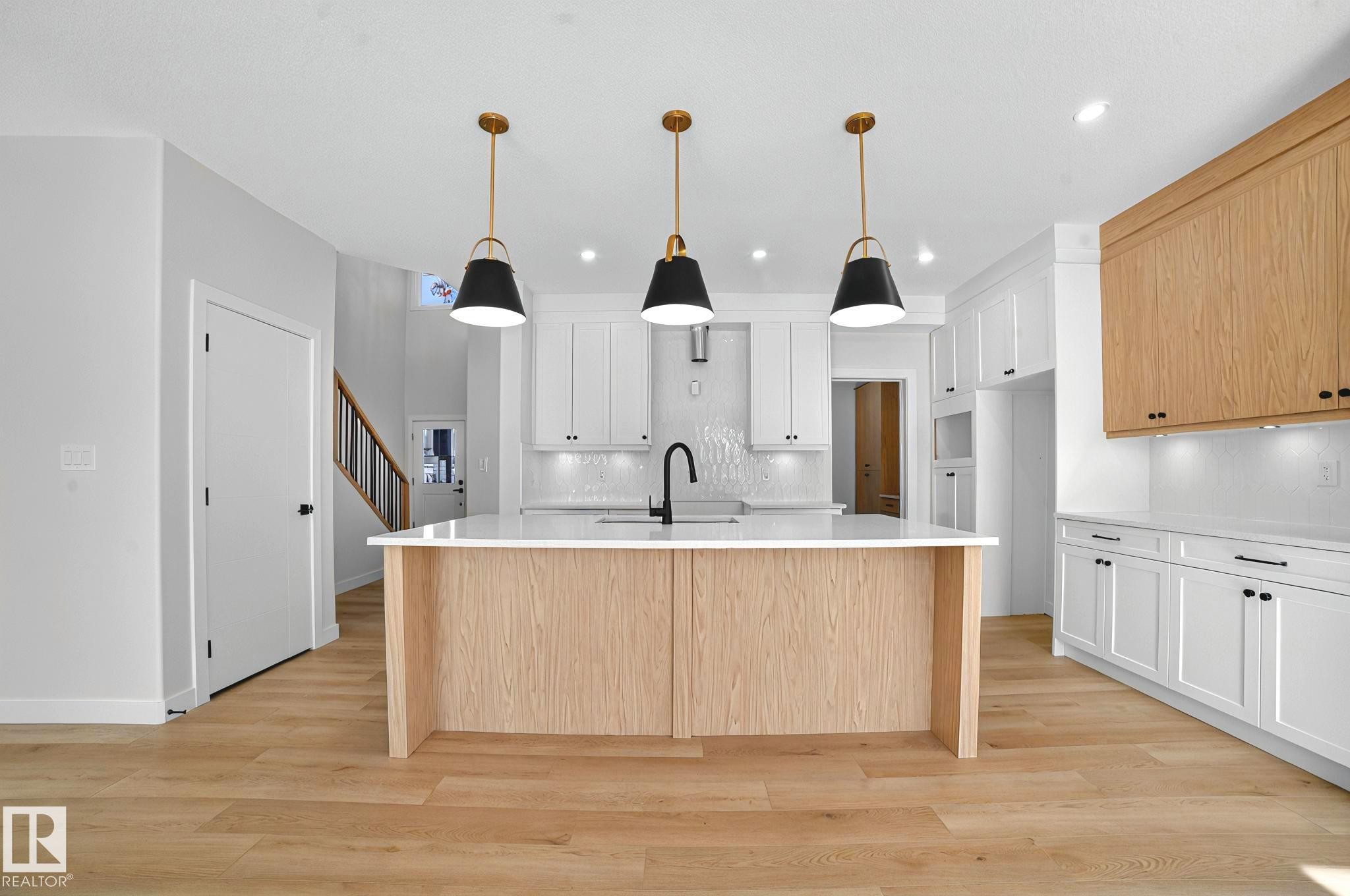 Dual tone kitchen featuring a large island with sink, two tone cabinetry, light wood-style flooring, and light stone countertops - 523 Ashgrove Circle, Leduc, AB - Indoor Photo Showing Kitchen With Upgraded Kitchen