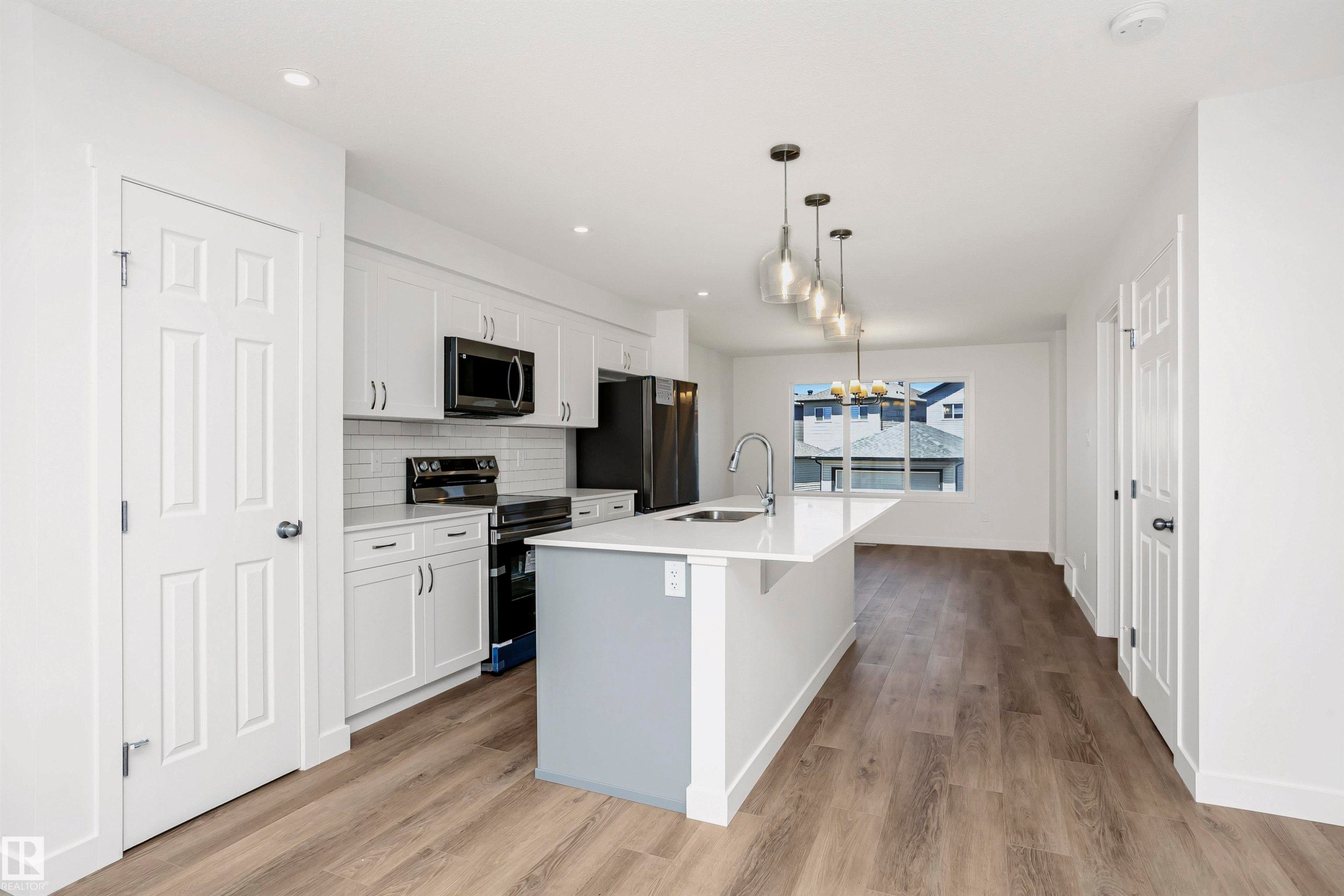 Kitchen with a chandelier, stainless steel appliances, white cabinetry, a center island with sink, and light wood finished floors - 9552 Carson Bend, Edmonton, AB - Indoor Photo Showing Kitchen