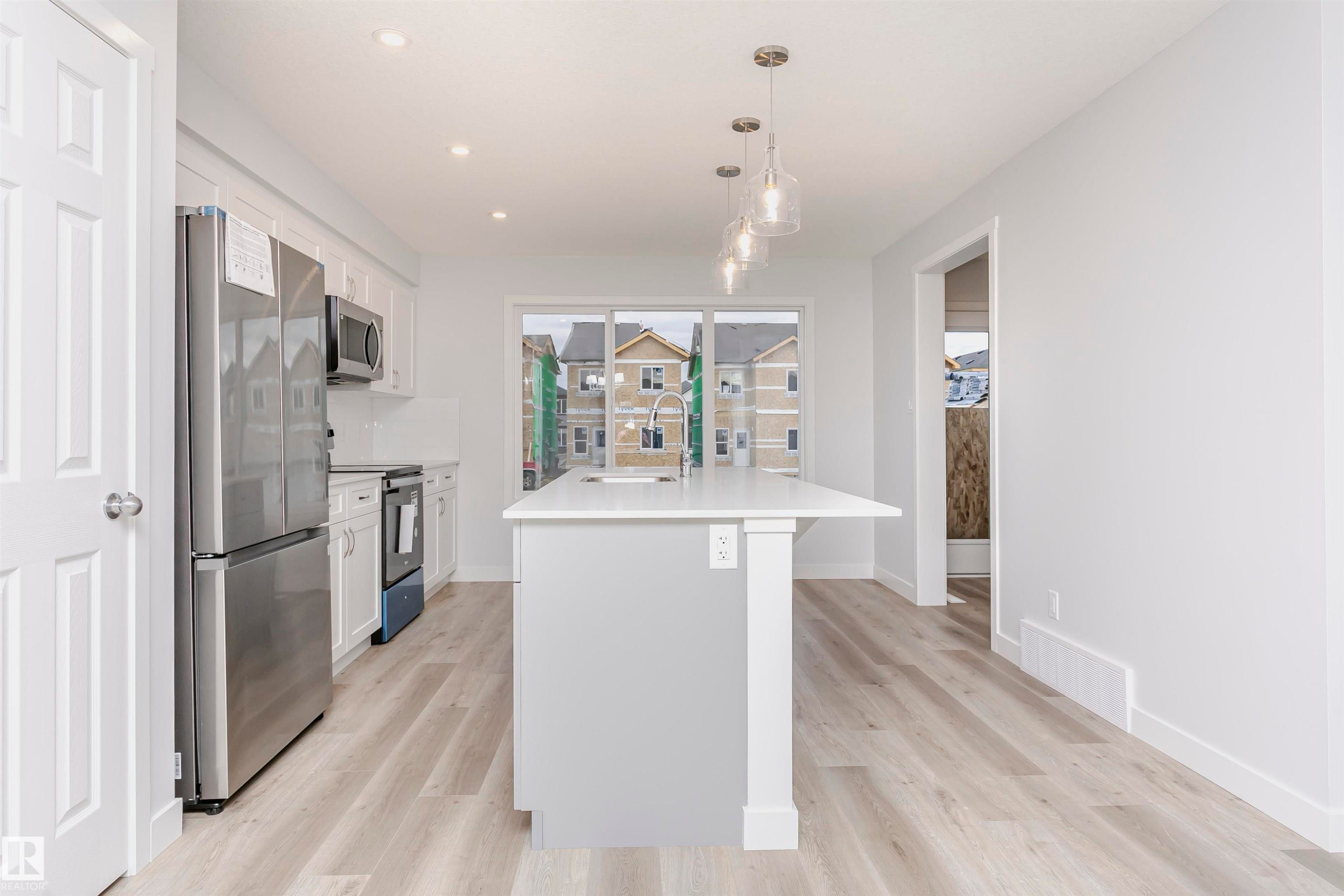 Kitchen with an island with sink, white cabinetry, stainless steel appliances, and light wood-style flooring - 9564 Carson Bend, Edmonton, AB - Indoor Photo Showing Kitchen With Upgraded Kitchen