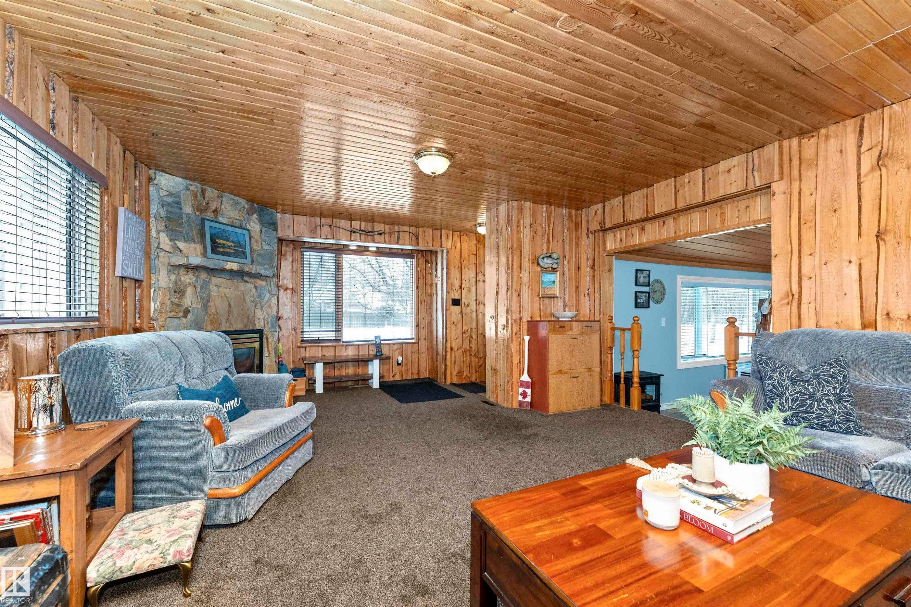 Carpeted living room featuring healthy amount of natural light, wood walls, and wooden ceiling - 516 5 Street, Rural Lac Ste. Anne County, AB - Indoor Photo Showing Living Room