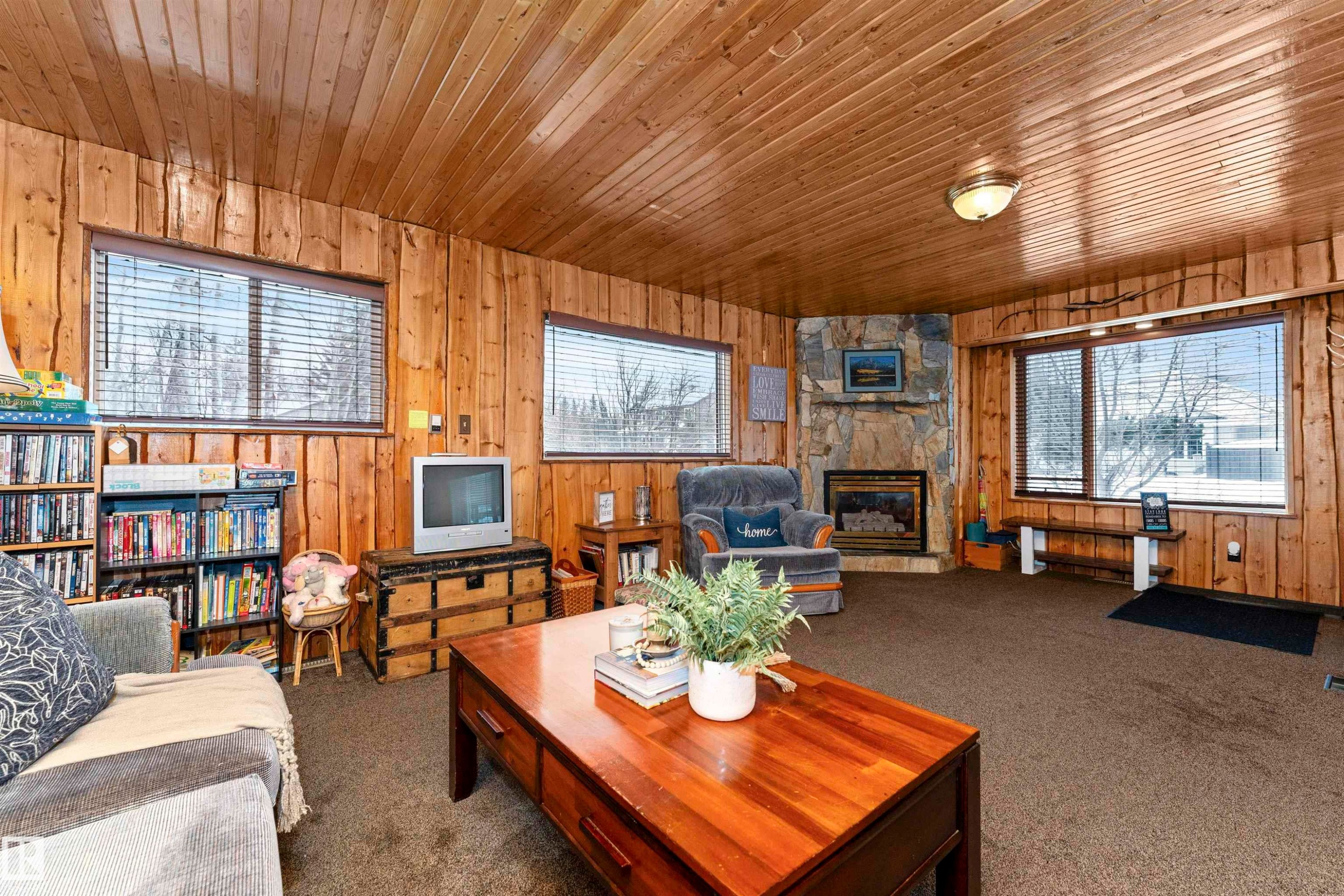 Living area featuring wood walls, carpet flooring, a stone fireplace, and wooden ceiling - 516 5 Street, Rural Lac Ste. Anne County, AB - Indoor With Fireplace