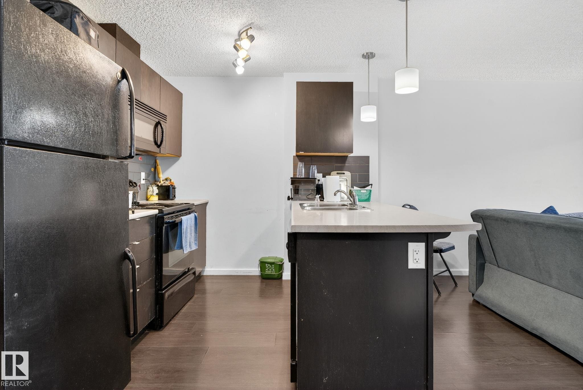 Kitchen with black appliances, open floor plan, dark wood-type flooring, a kitchen breakfast bar, and a textured ceiling - 209 3353 16A, Edmonton, AB - Indoor Photo Showing Kitchen