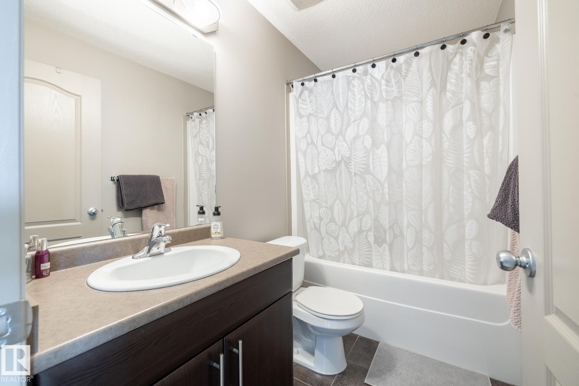 Full bath featuring vanity, shower / bathtub combination with curtain, a textured ceiling, and dark tile patterned floors - 3312 17B Avenue, Edmonton, AB - Indoor Photo Showing Bathroom
