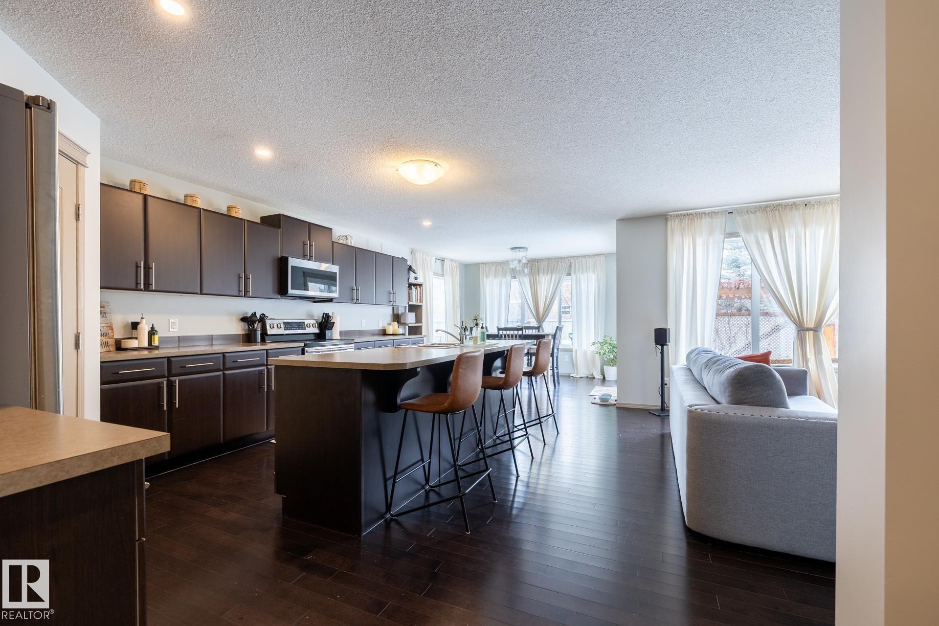 Kitchen with a center island with sink, dark wood finish cabinets, a breakfast bar area, stainless steel appliances, and a textured ceiling - 3312 17B Avenue, Edmonton, AB - Indoor Photo Showing Kitchen