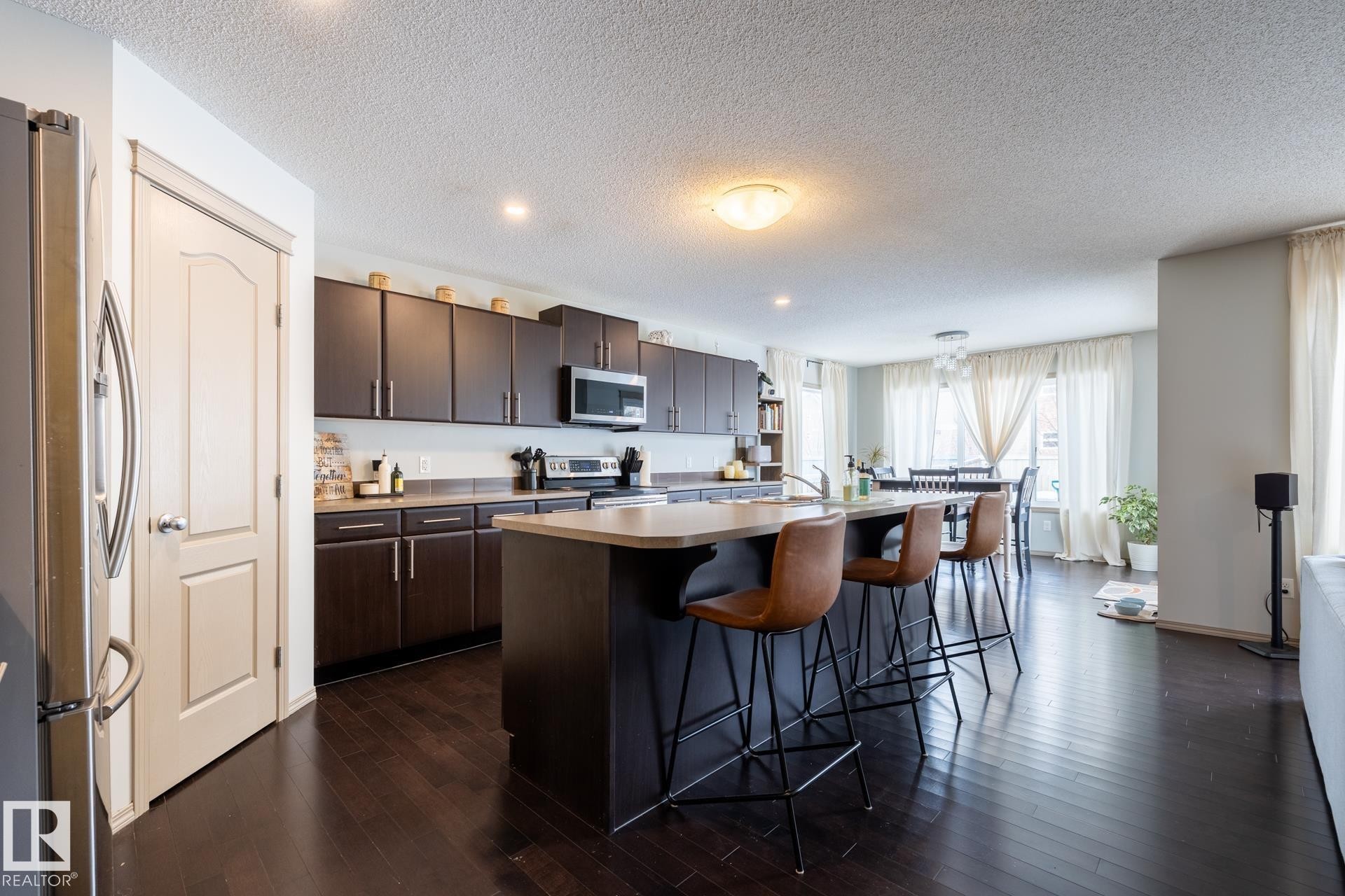 Kitchen with dark wood finish cabinetry, stainless steel appliances, dark wood finished floors, a breakfast bar, and a textured ceiling - 3312 17B Avenue, Edmonton, AB - Indoor Photo Showing Kitchen