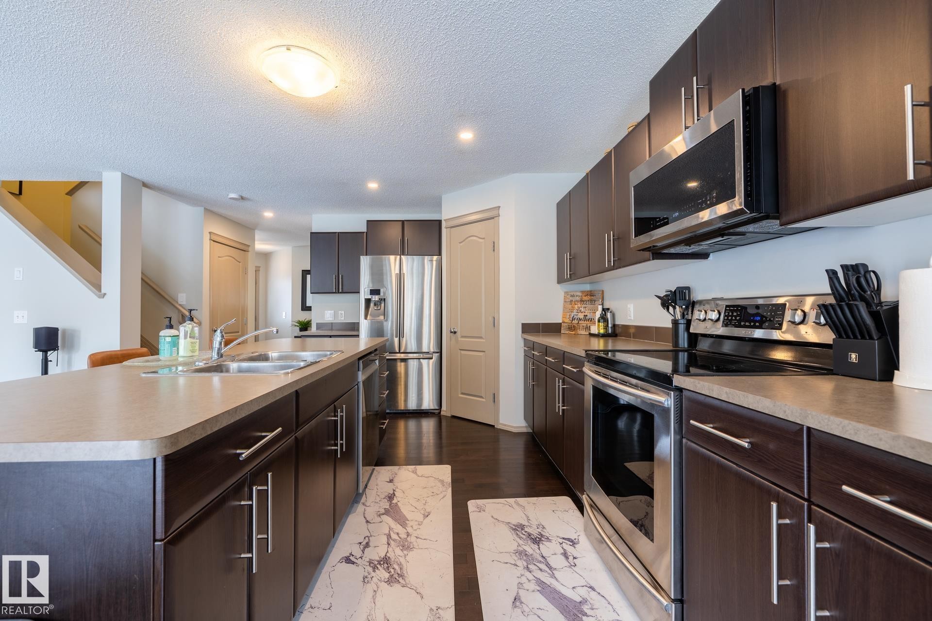 Kitchen with stainless steel appliances, a center island with sink, dark wood finish cabinets, a textured ceiling, and recessed lighting - 3312 17B Avenue, Edmonton, AB - Indoor Photo Showing Kitchen With Double Sink